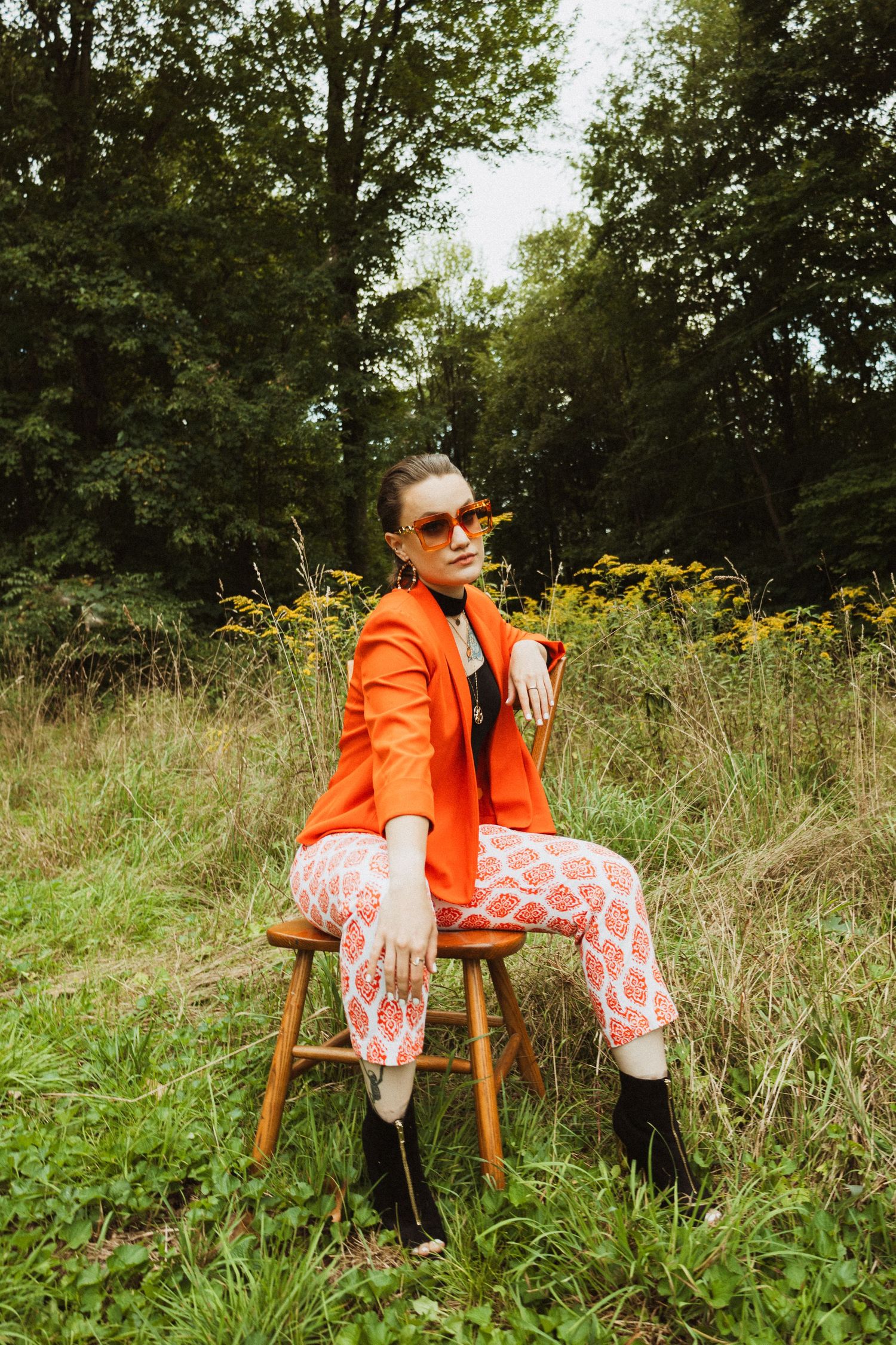 Retro fashion editorial featuring orange blazer and patterned pants on rustic wooden stool.