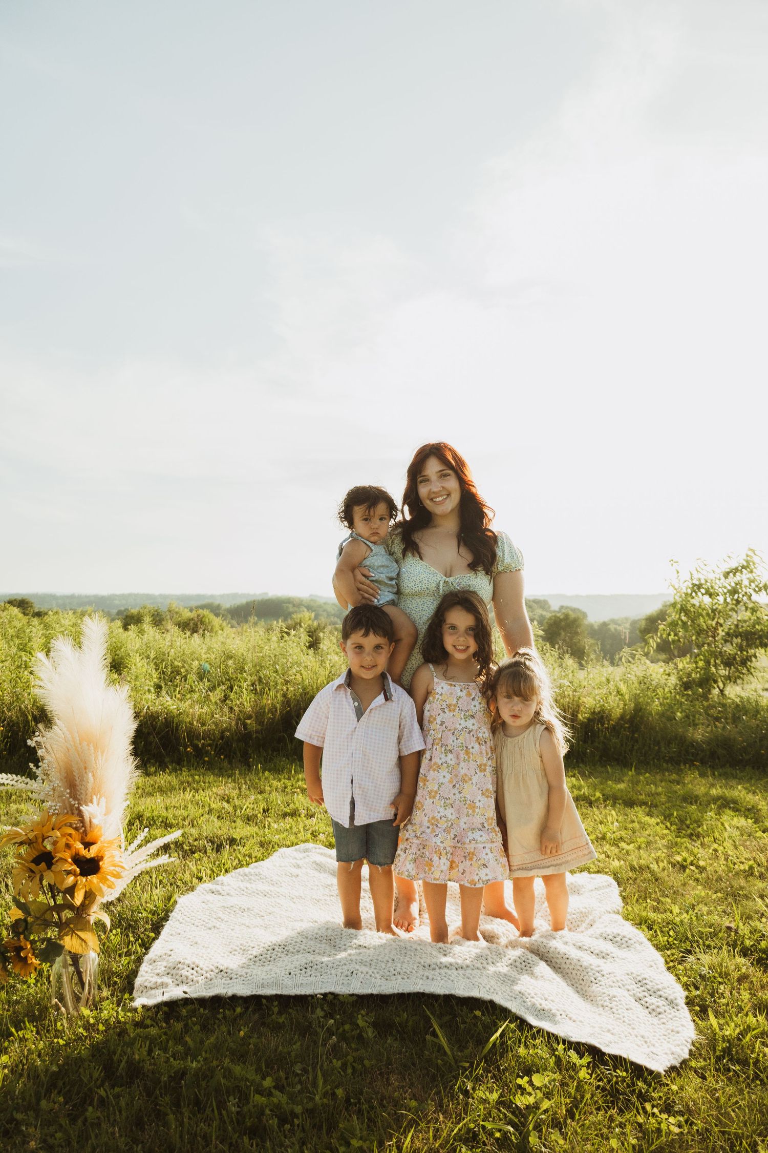 A family sits together on a white blanket in a sunlit meadow on a summer afternoon.