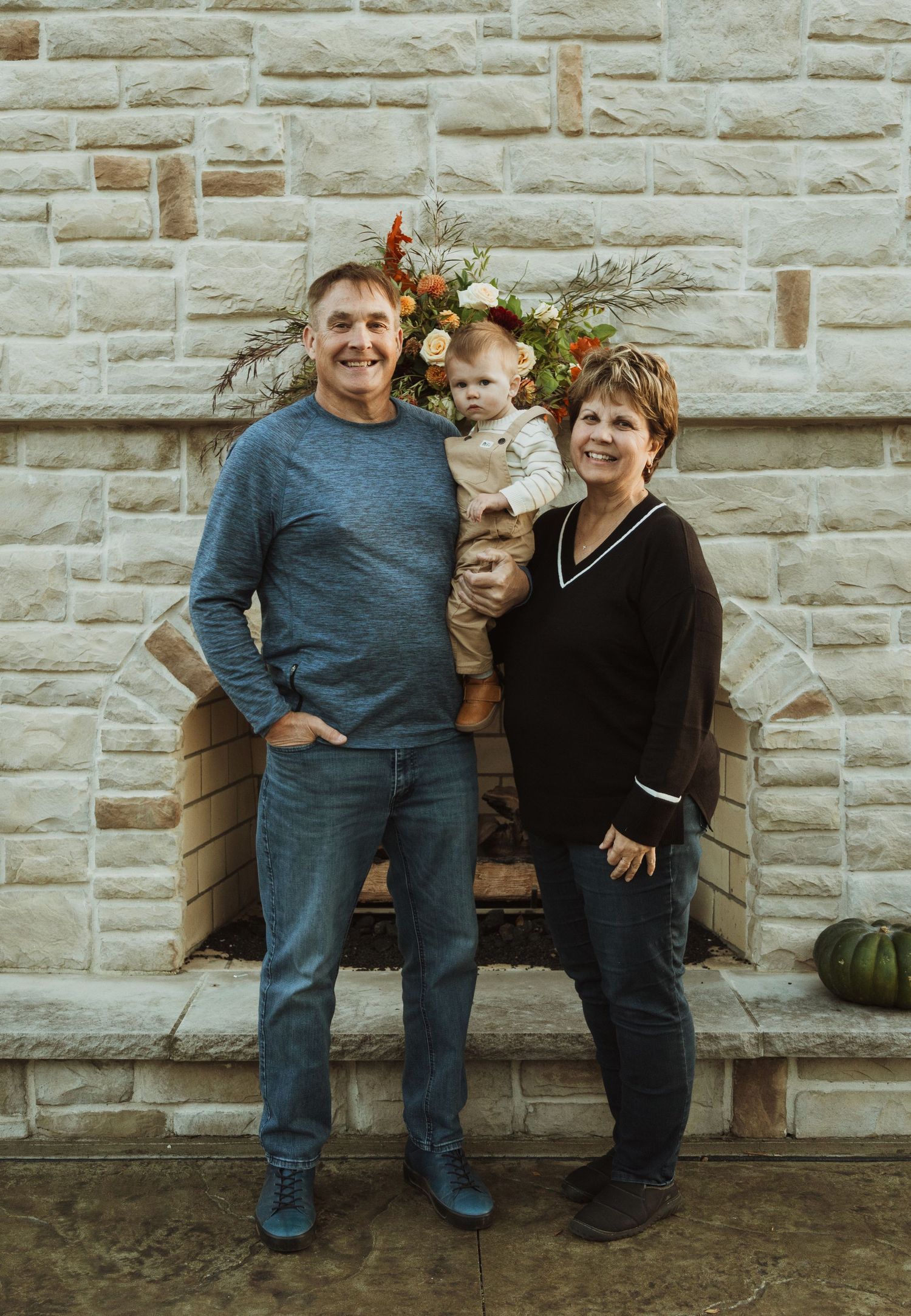Family poses together against a stone wall decorated with autumn floral arrangements.