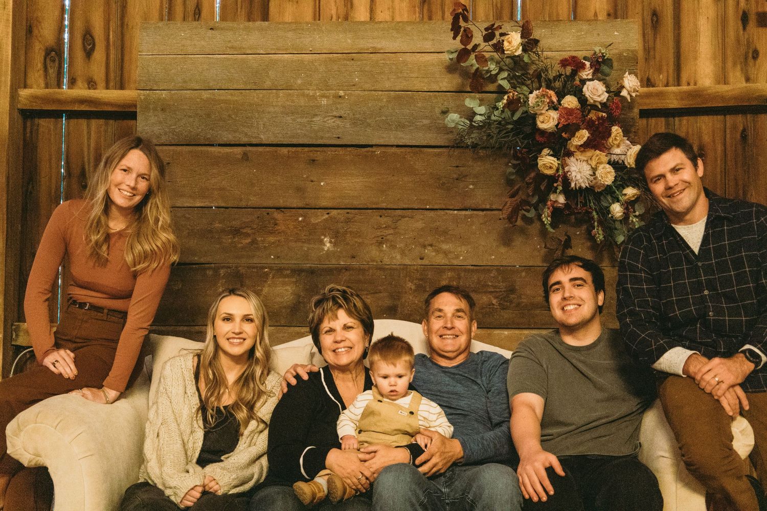 Extended family portrait in rustic barn setting with wooden walls and floral arrangements.