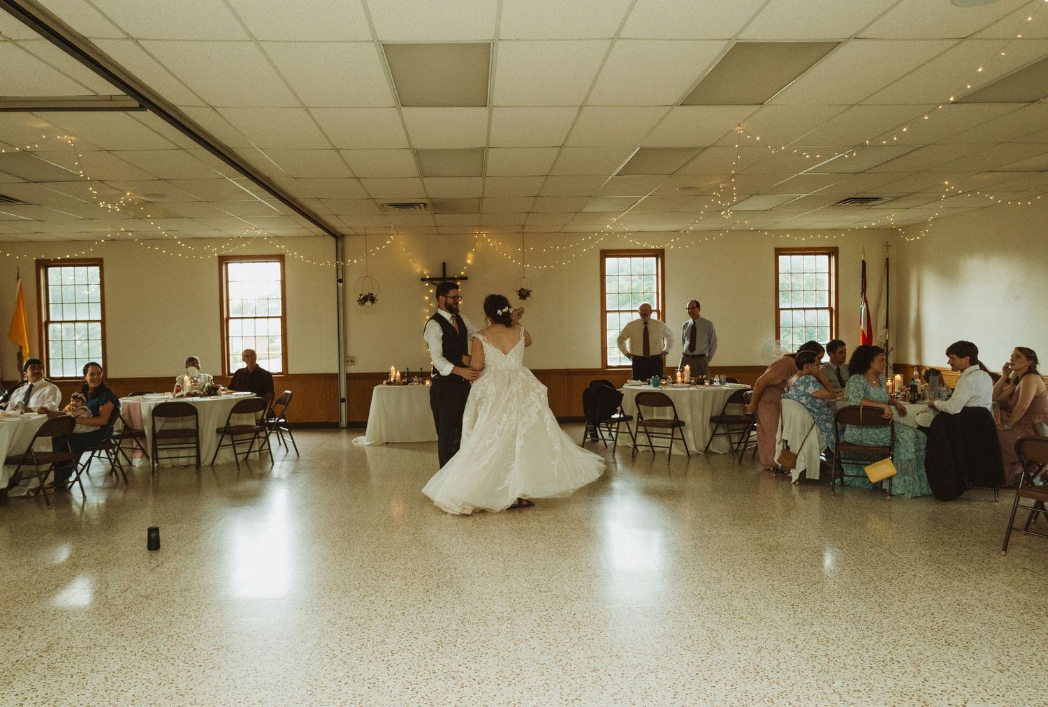 A panoramic view of a dance lesson in progress inside a large community hall with hardwood floors and chairs along the walls.