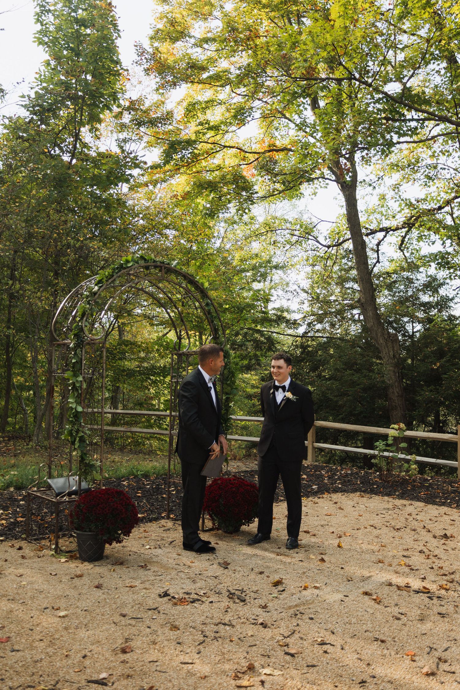 Wedding party gathered in wooded outdoor ceremony space with fall leaves on ground.