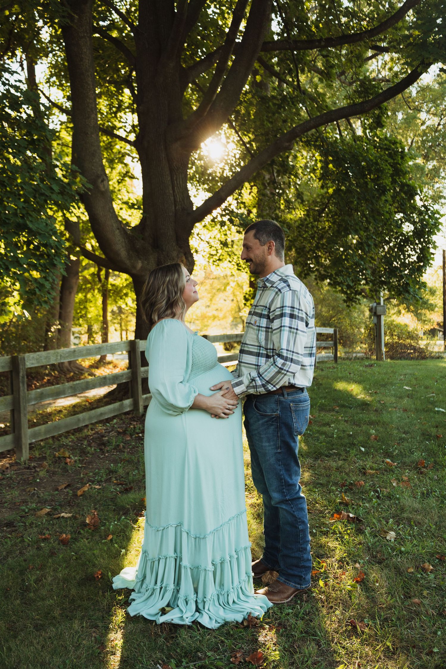 A couple shares a tender moment in front of a rustic wooden fence during a golden sunset in the countryside.