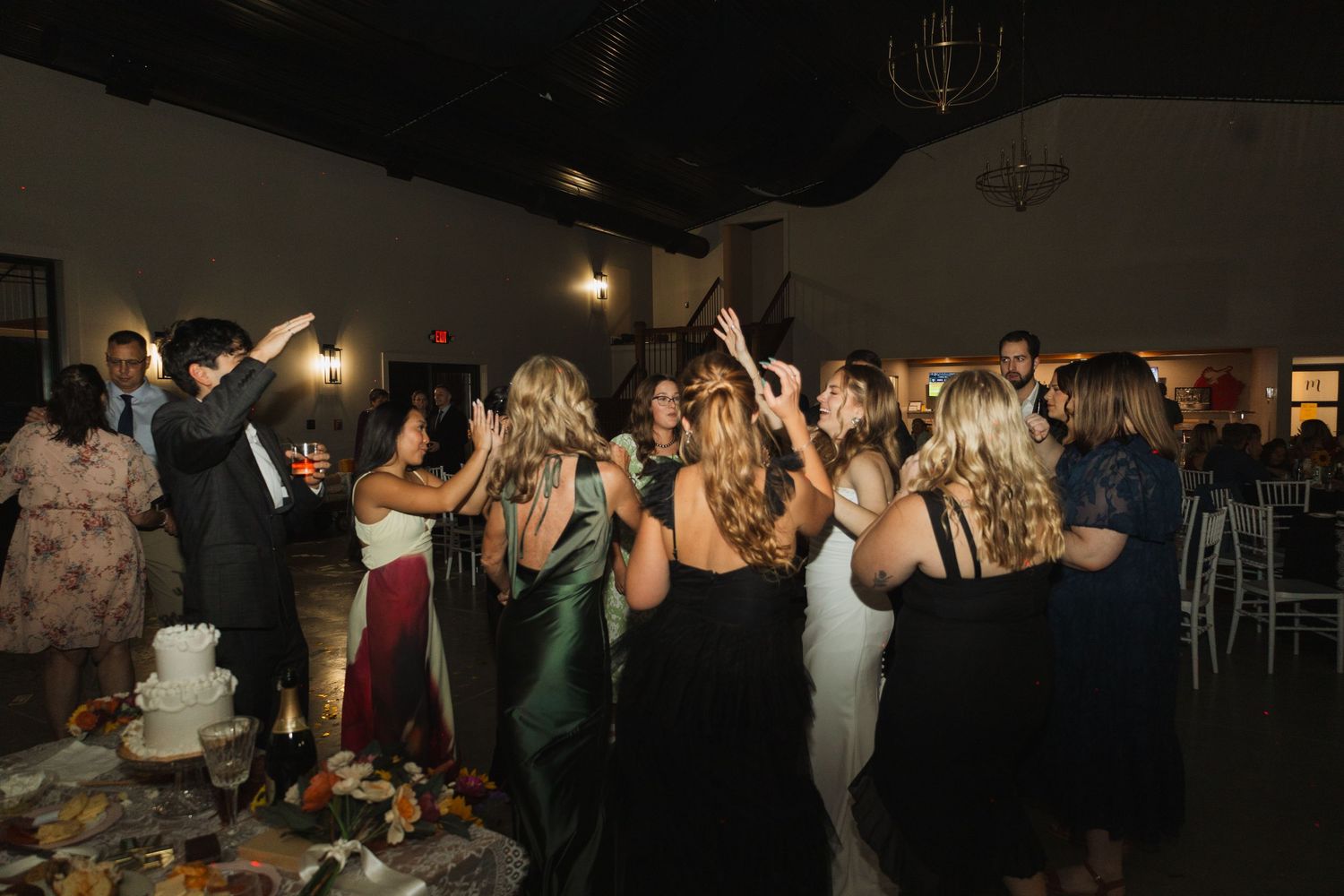 Wedding guests celebrate on dance floor during evening reception in elegant ballroom setting.