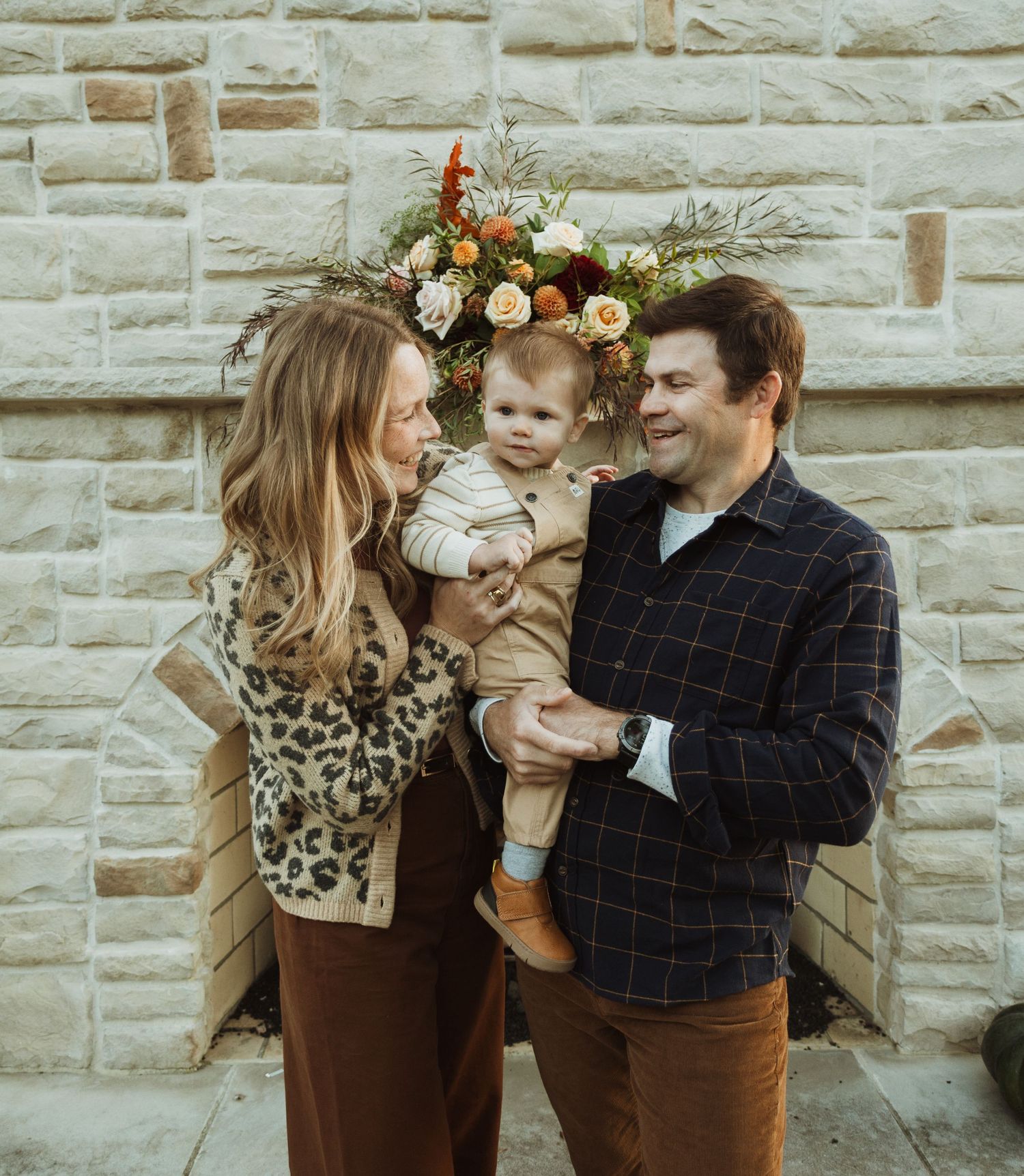 Family shares intimate moment in front of stone wall with floral decorations.