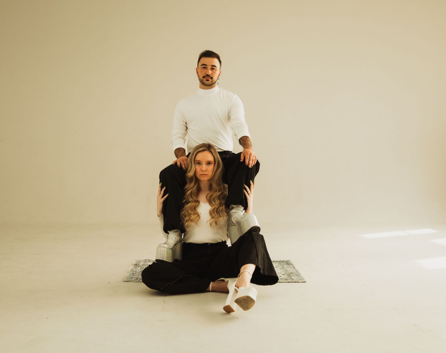 Two people pose together on a minimalist white studio background while sitting on a textured rug.