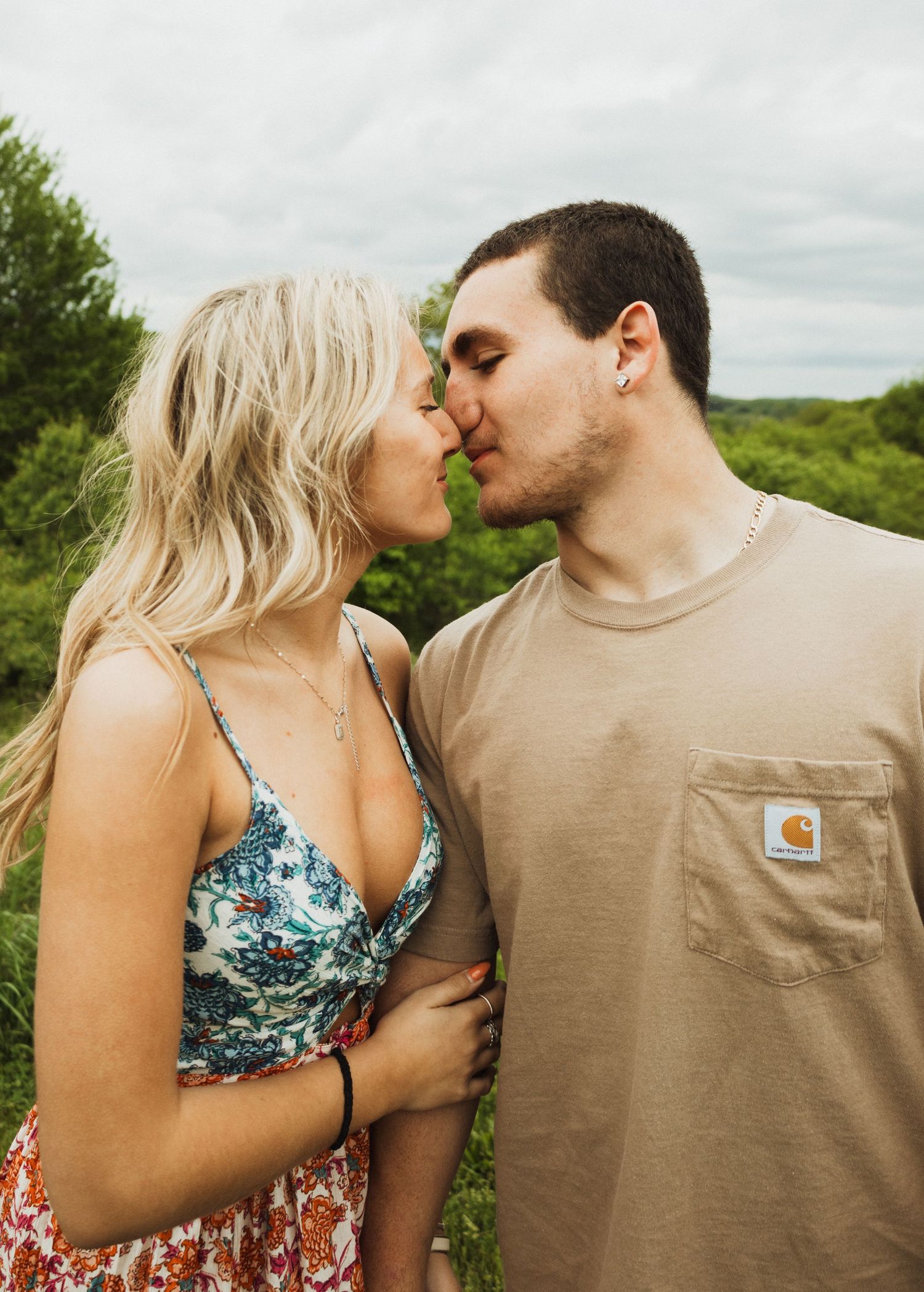 A romantic couple sharing an intimate moment on a hillside with green foliage in the background.