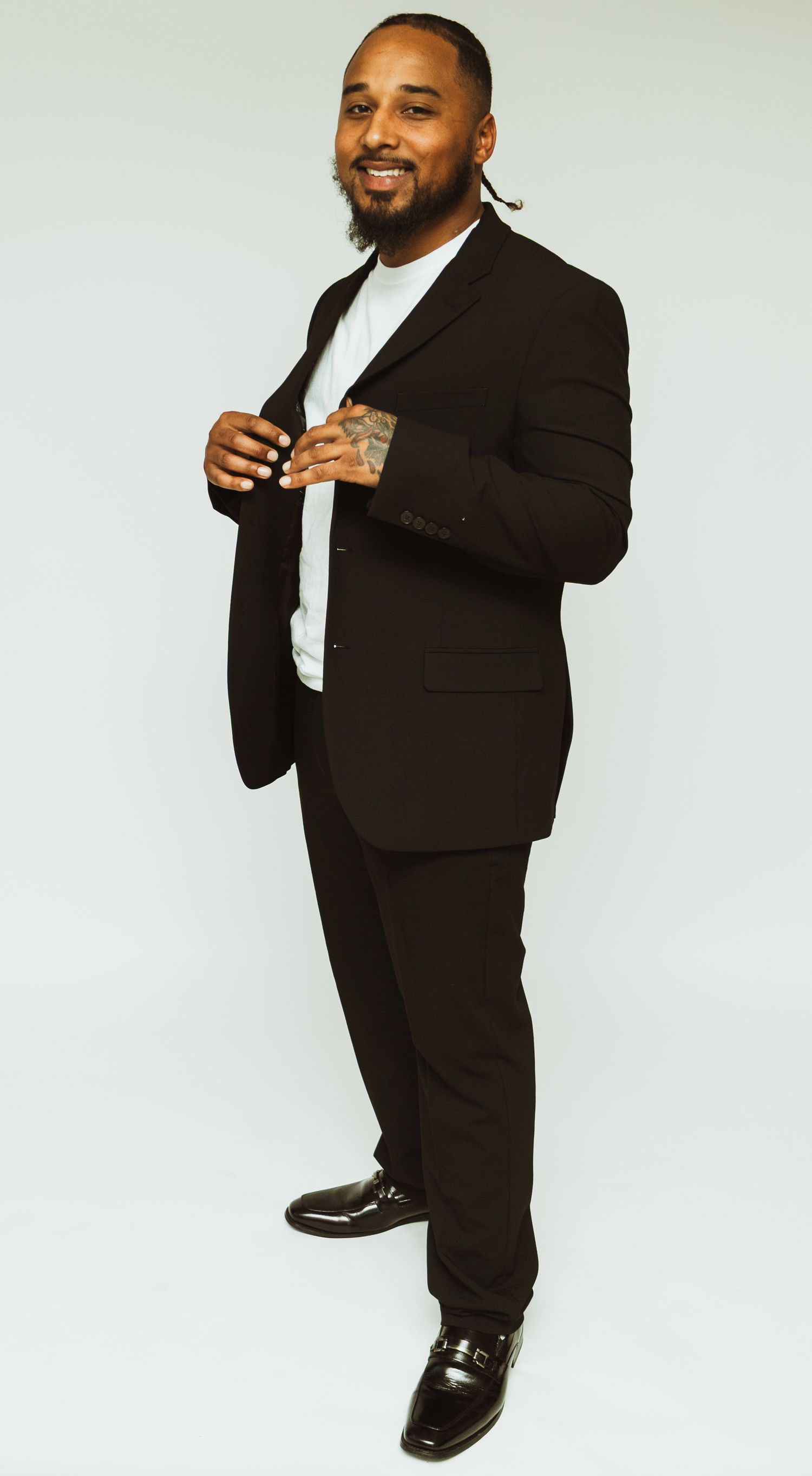 Candid portrait of someone in a black suit and white shirt smiling warmly against a minimal background.