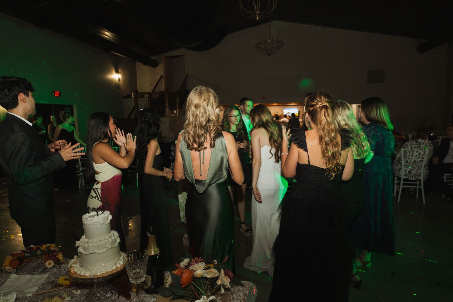 Wedding guests dancing and celebrating at a dimly lit reception venue.