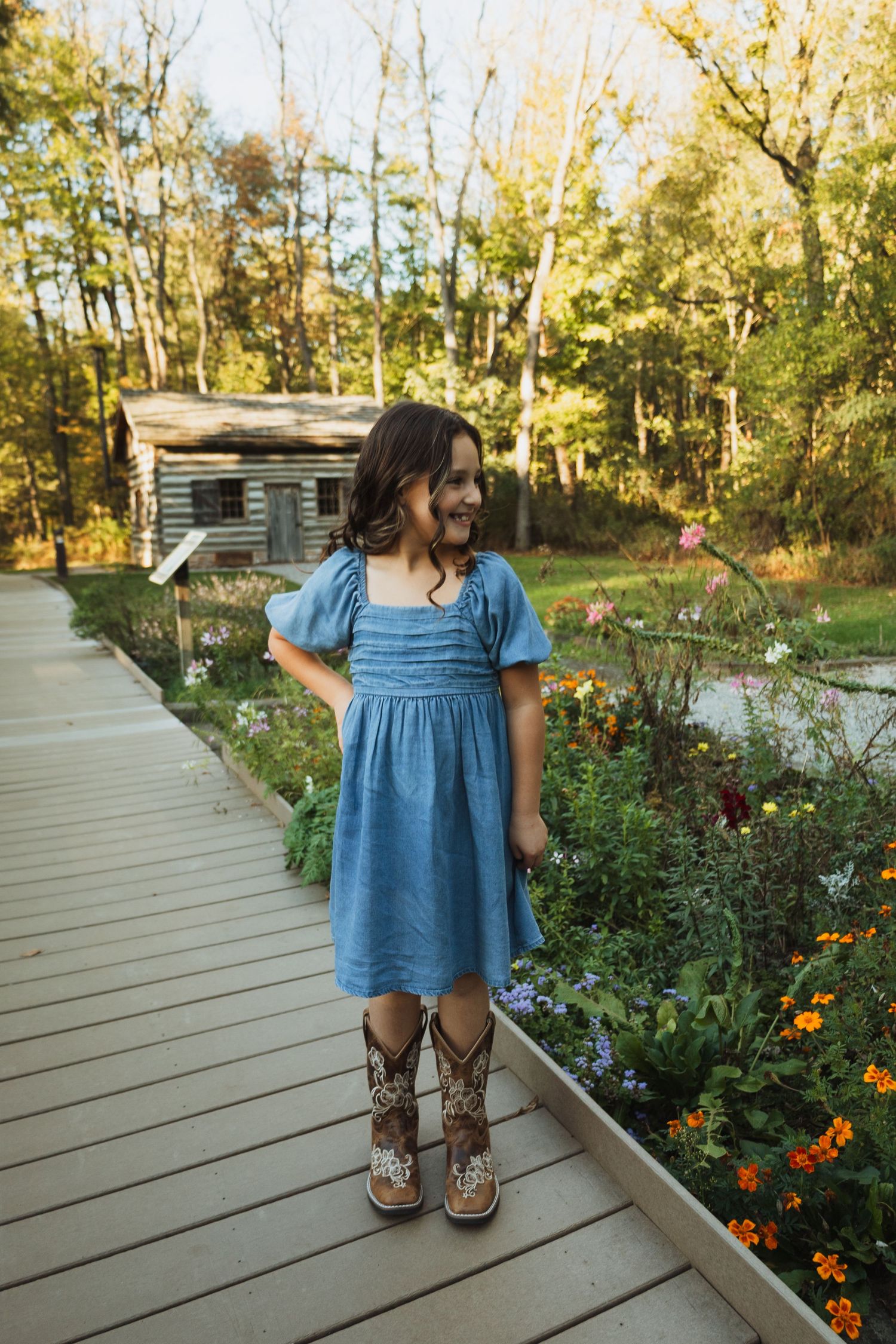 A series of photos showing someone in a blue dress and brown boots standing on a wooden deck near blooming flowers.