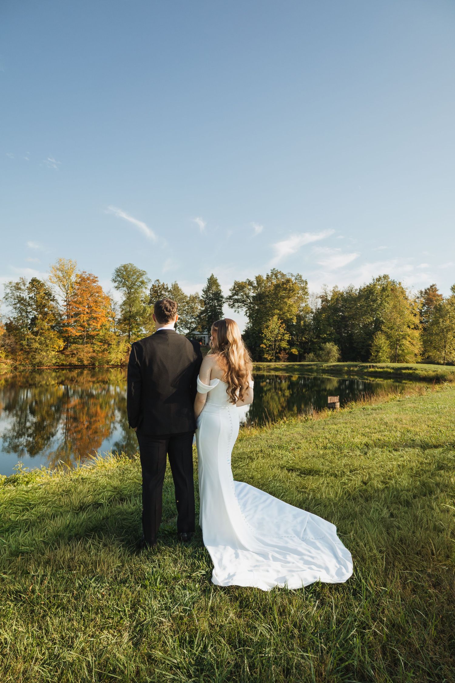 Wedding couple overlooking a serene lake surrounded by autumn trees during golden hour.