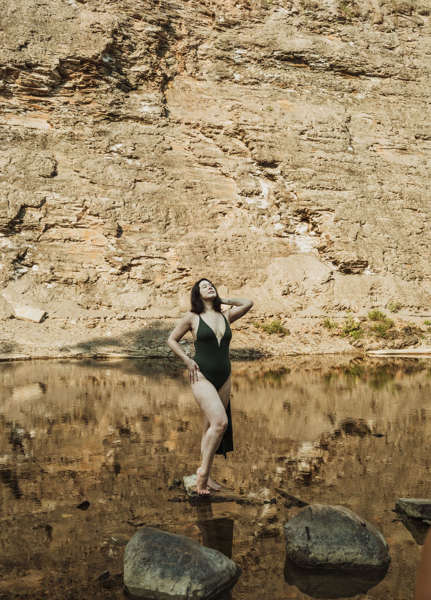 A series of photos showing someone balancing on rocks near a rocky cliff wall reflected in still water.