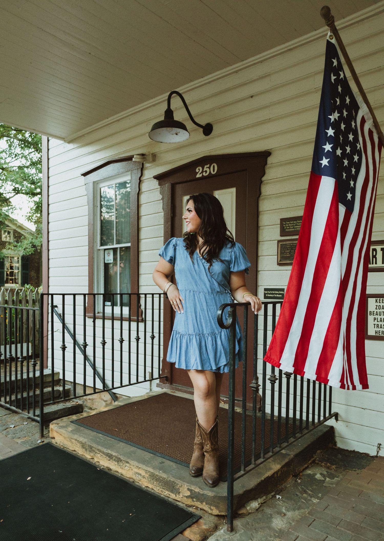 A covered front porch of a white house with American flags displayed and black metal railings.