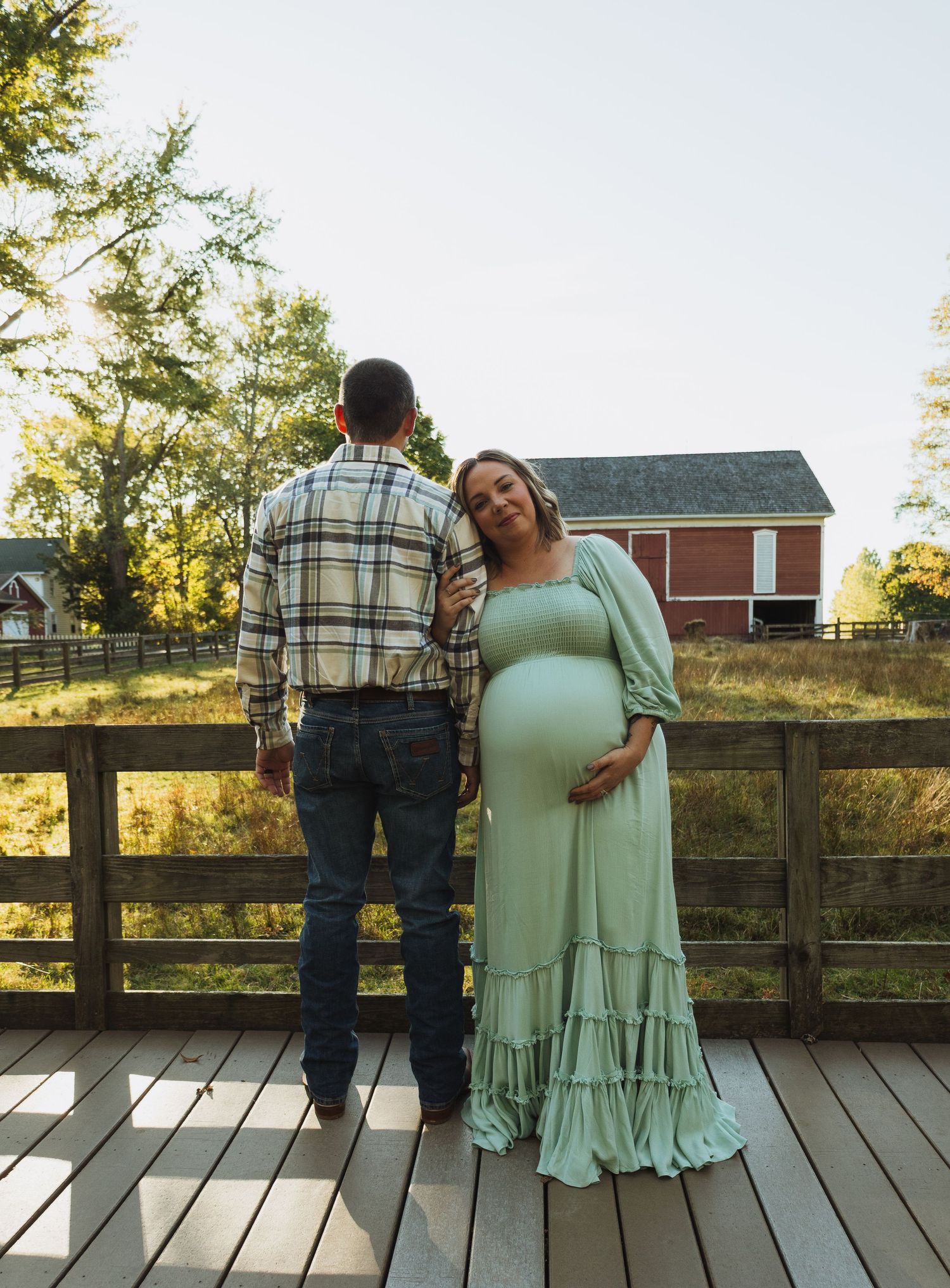 A couple shares a tender moment on a wooden deck at sunset with a rustic barn and trees in the background.