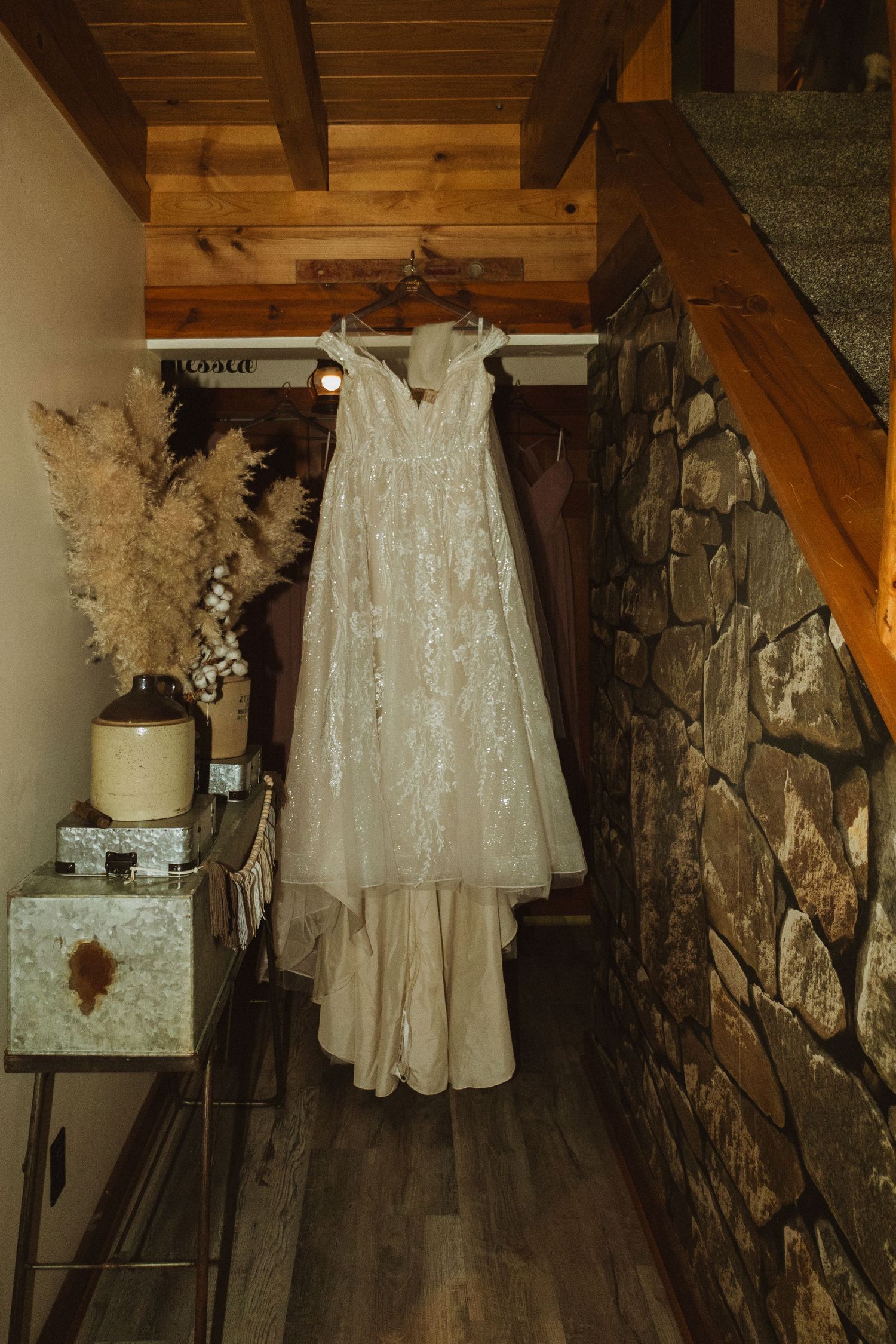 Elegant white wedding dress hanging in rustic wooden room with stone walls and vintage decor.