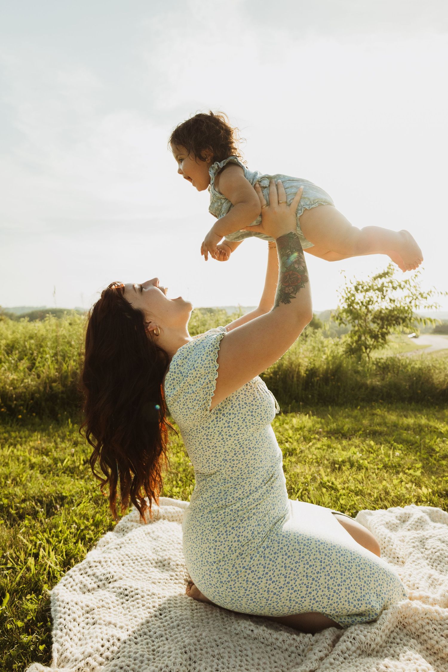 A heartwarming moment between parent and child playing together on a blanket outdoors in golden sunlight.