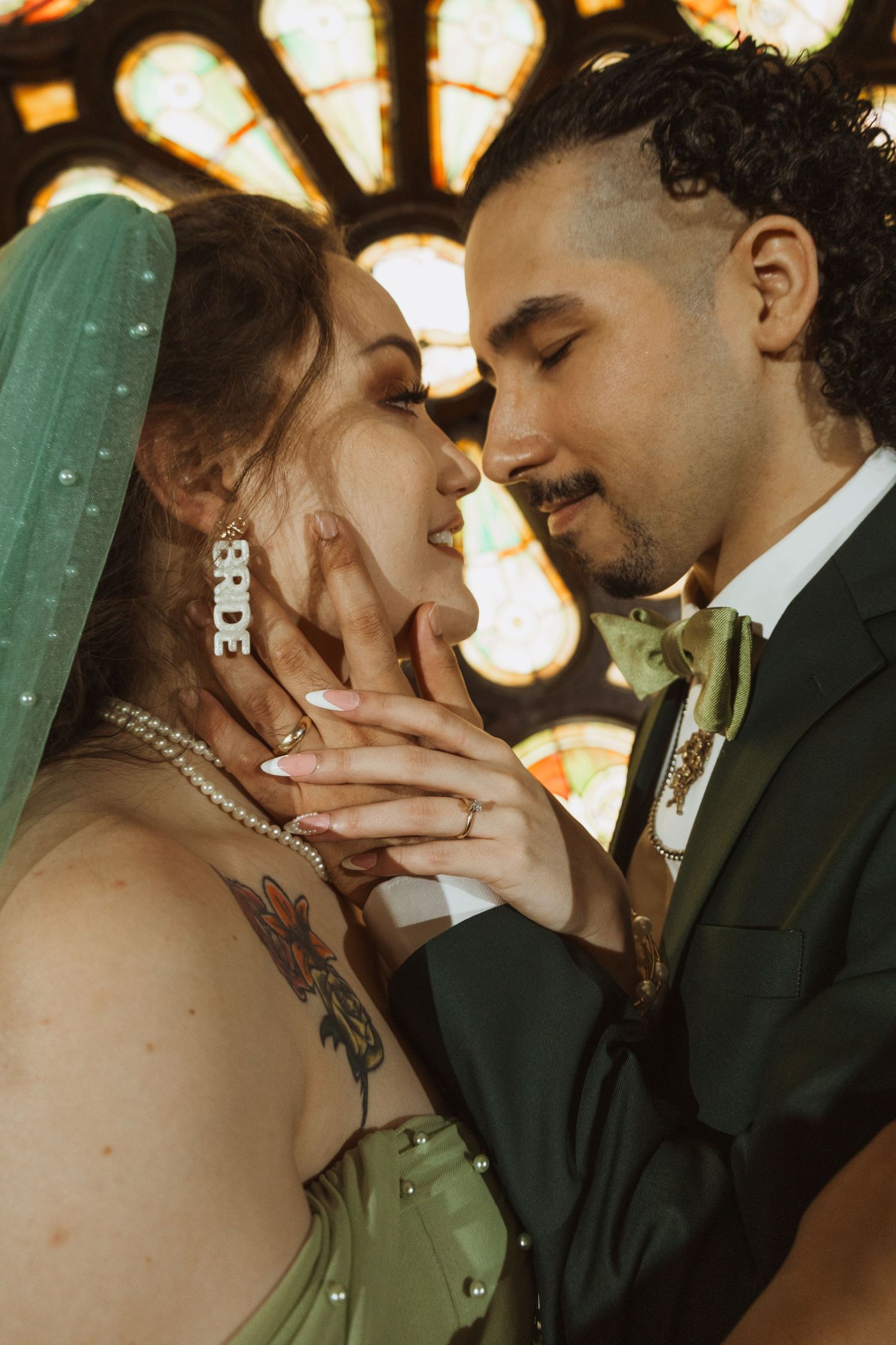 Bride and groom sharing an intimate moment before a colorful stained glass window in a church.