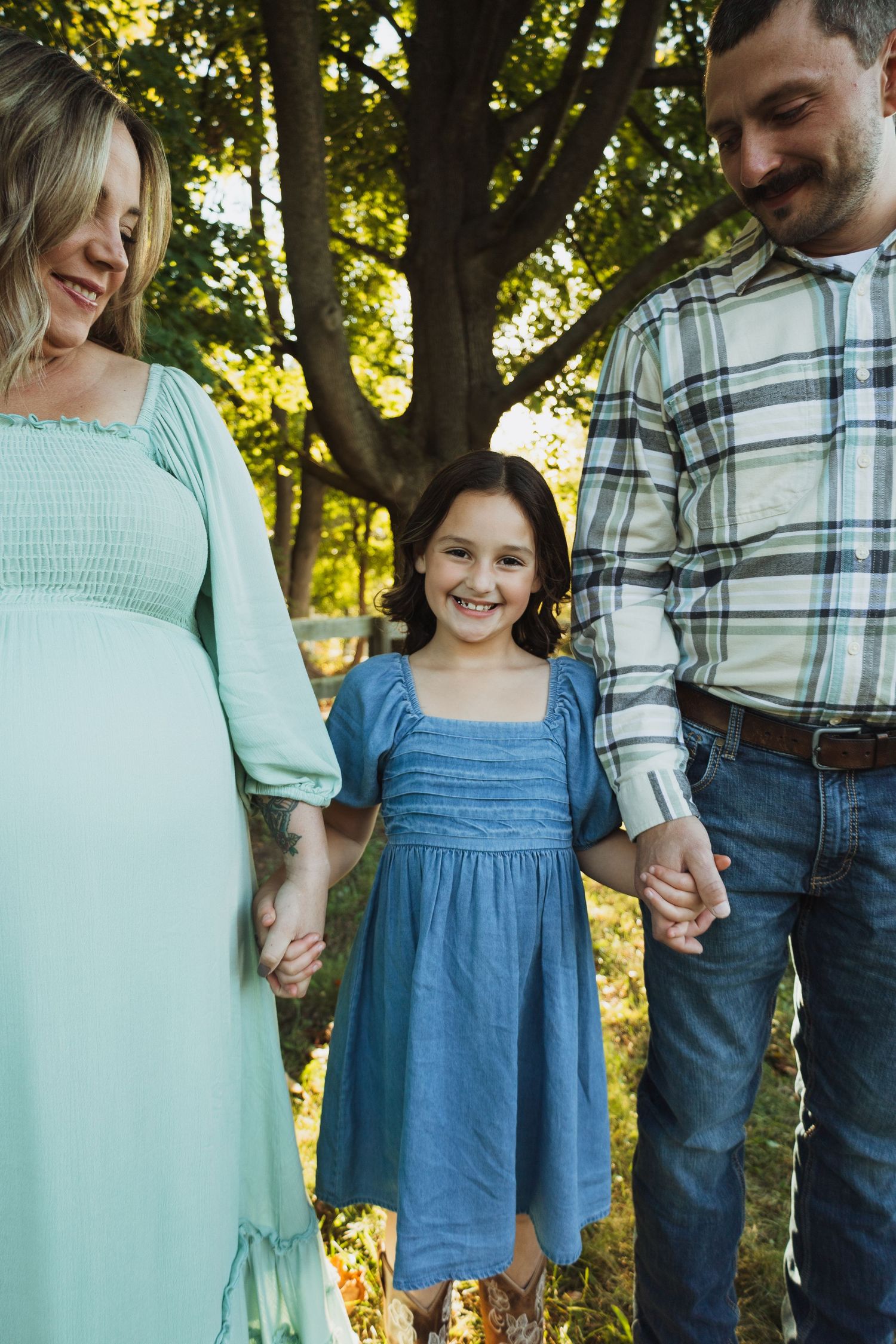 A family in coordinating mint green and blue outfits poses together outdoors in dappled sunlight.