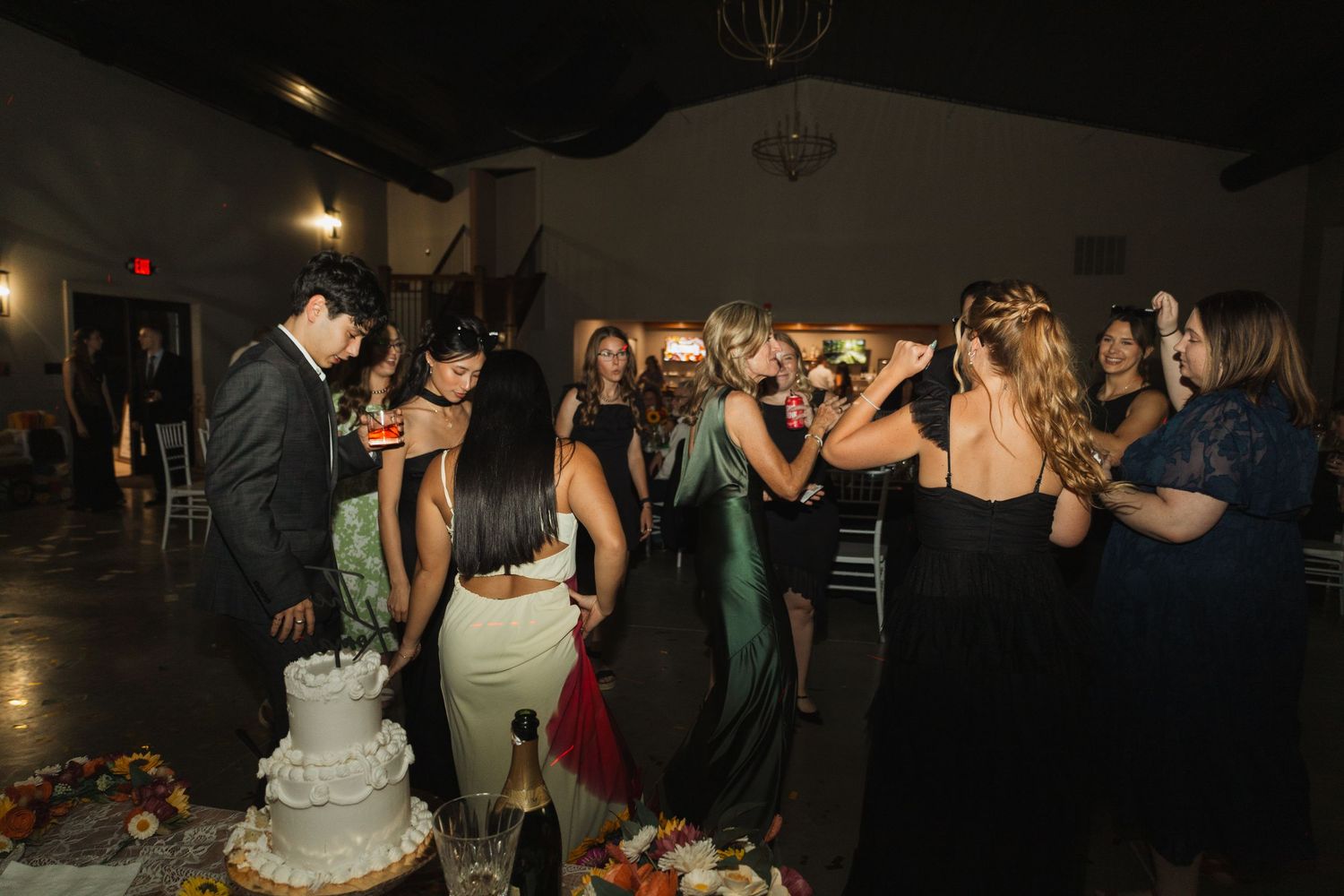 Wedding reception dance party with guests celebrating in a dimly lit venue.