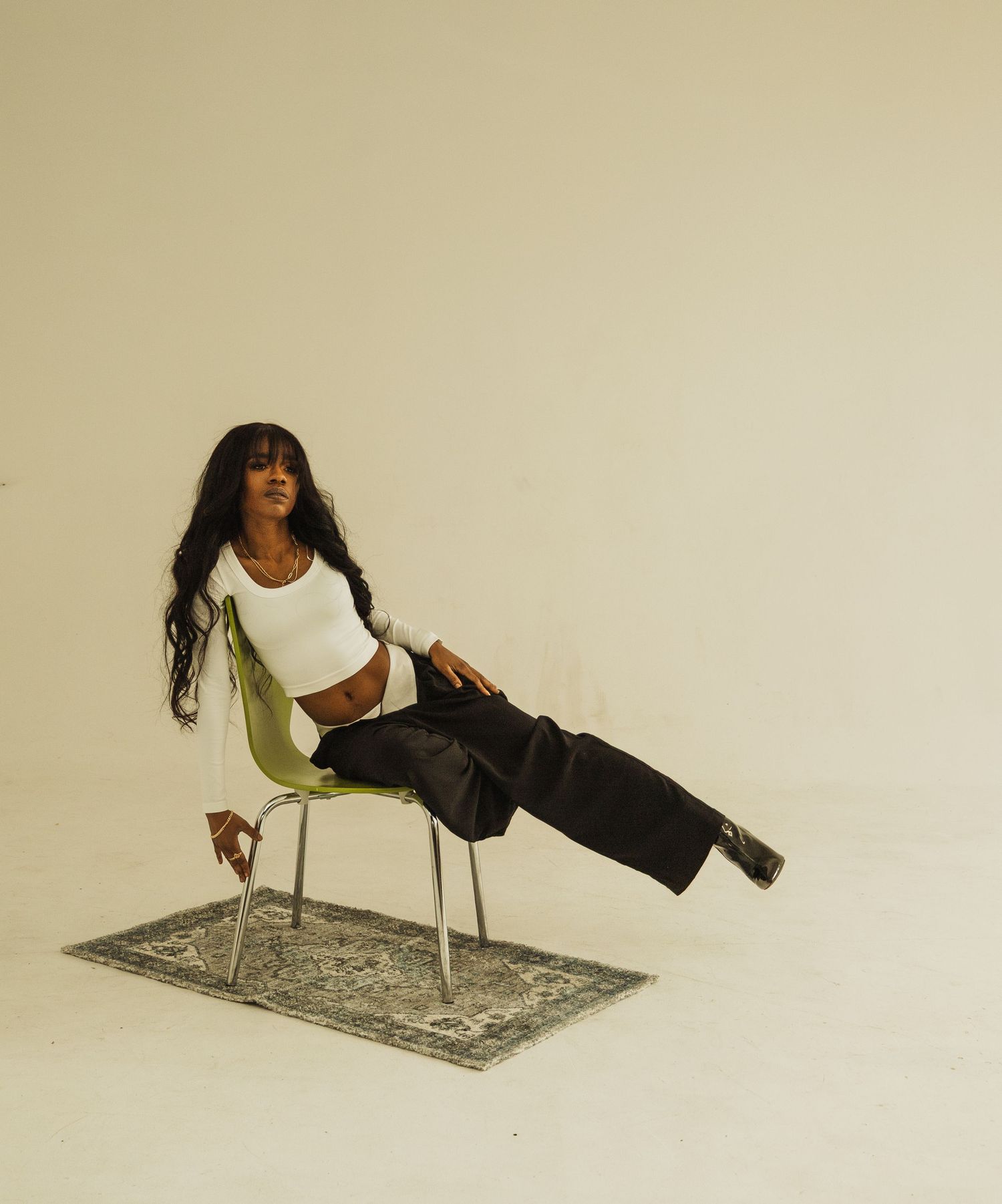 Person in white top and black pants posing on modern chair with decorative rug underneath.