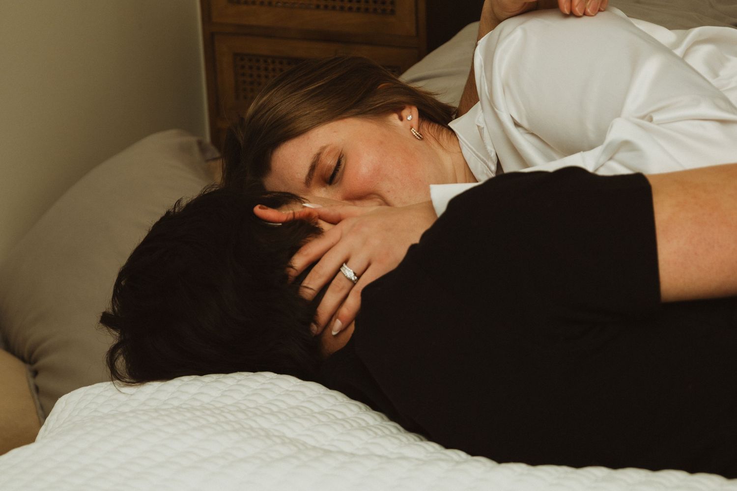 Couple sharing an intimate embrace while lying on white bedding.