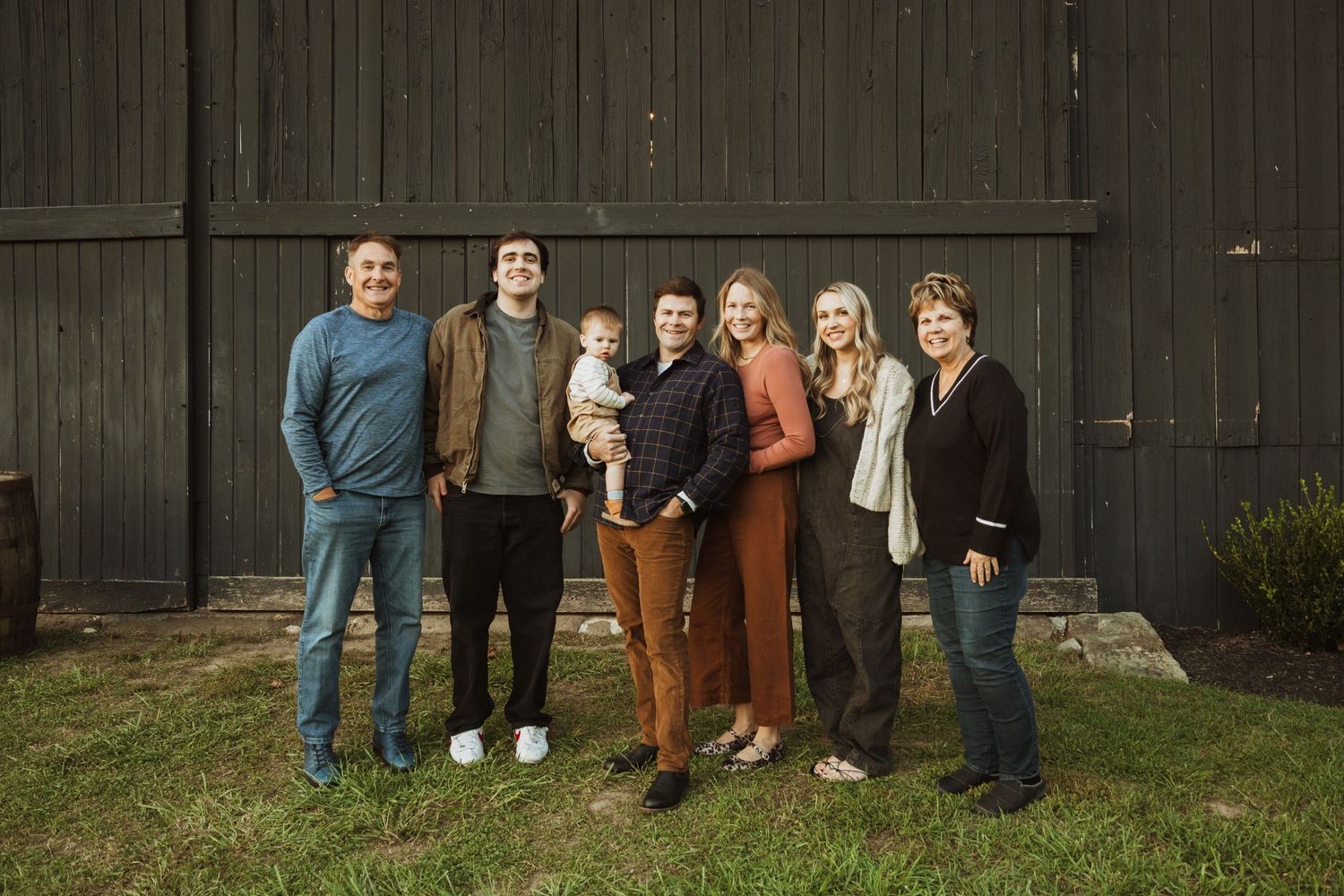 Family group photo against dark barn wall exterior in casual attire.