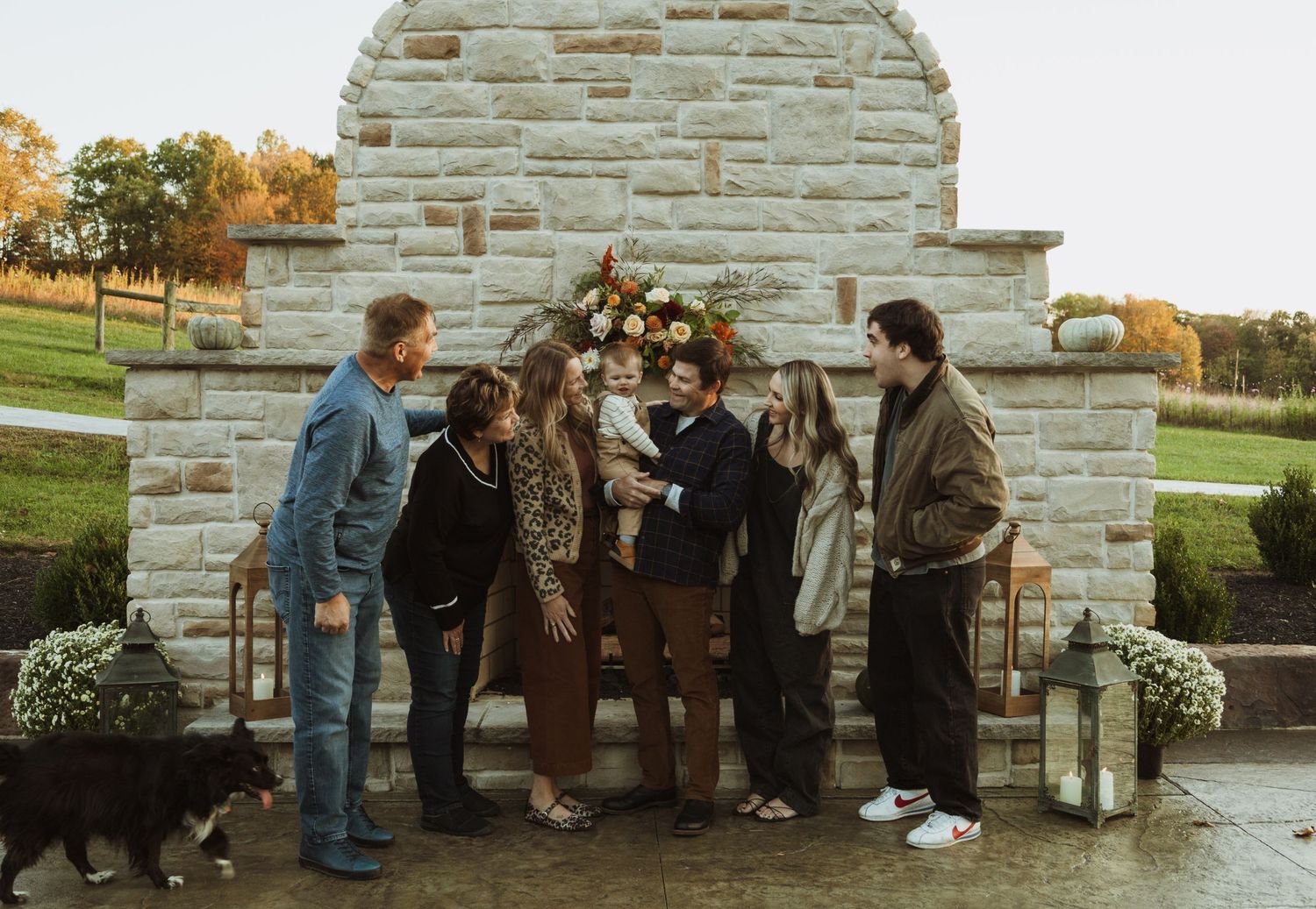 Group poses casually in front of a decorative stone fireplace with floral arrangements and lanterns.