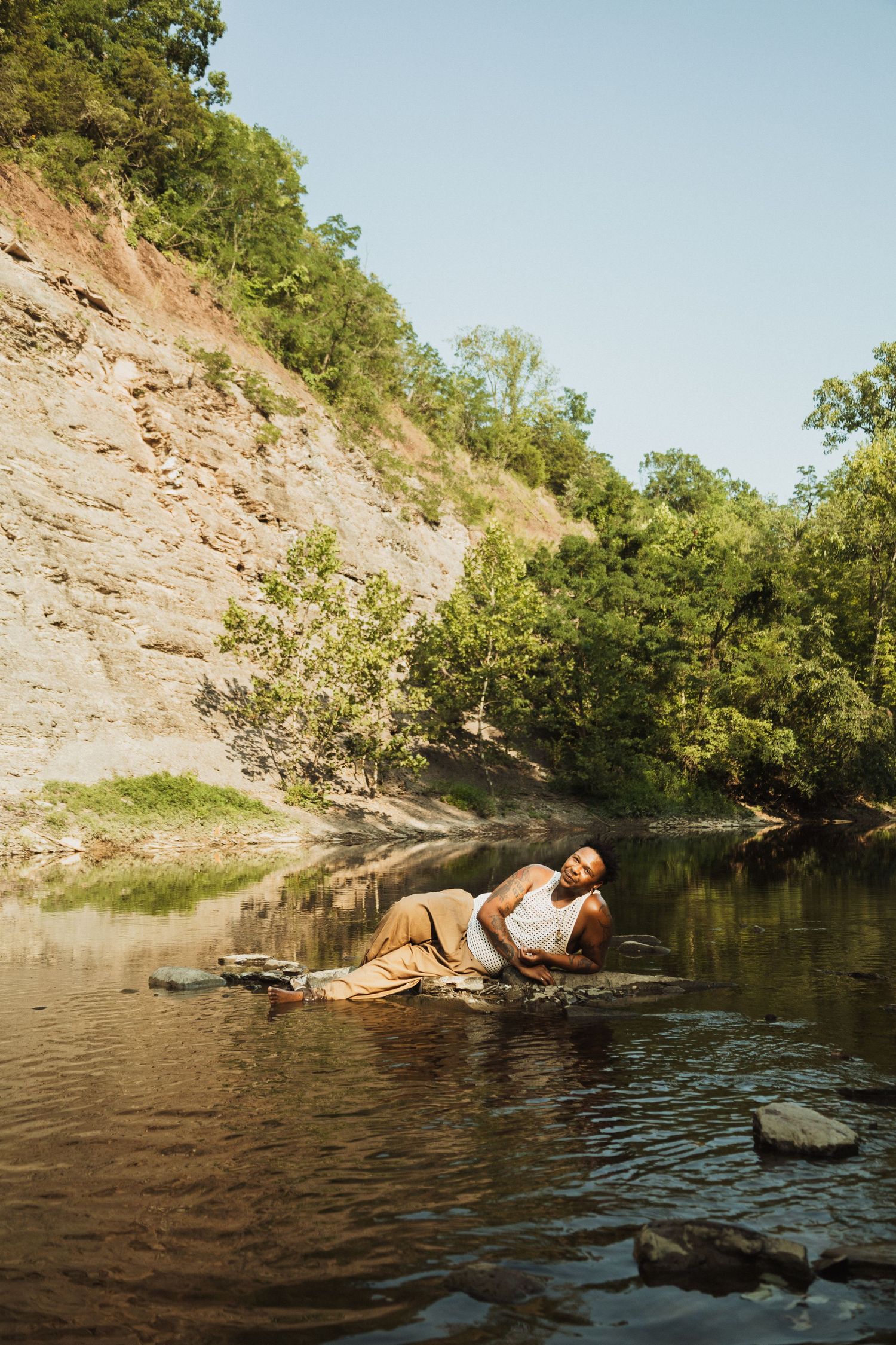 Person relaxing in a serene swimming hole surrounded by rocky cliffs and green trees.