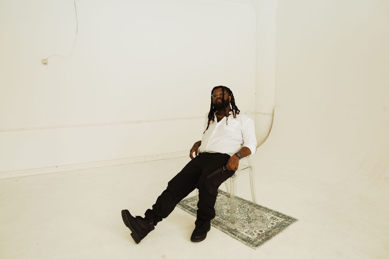 Person wearing white shirt and black pants lies casually on a white floor next to a decorative rug.
