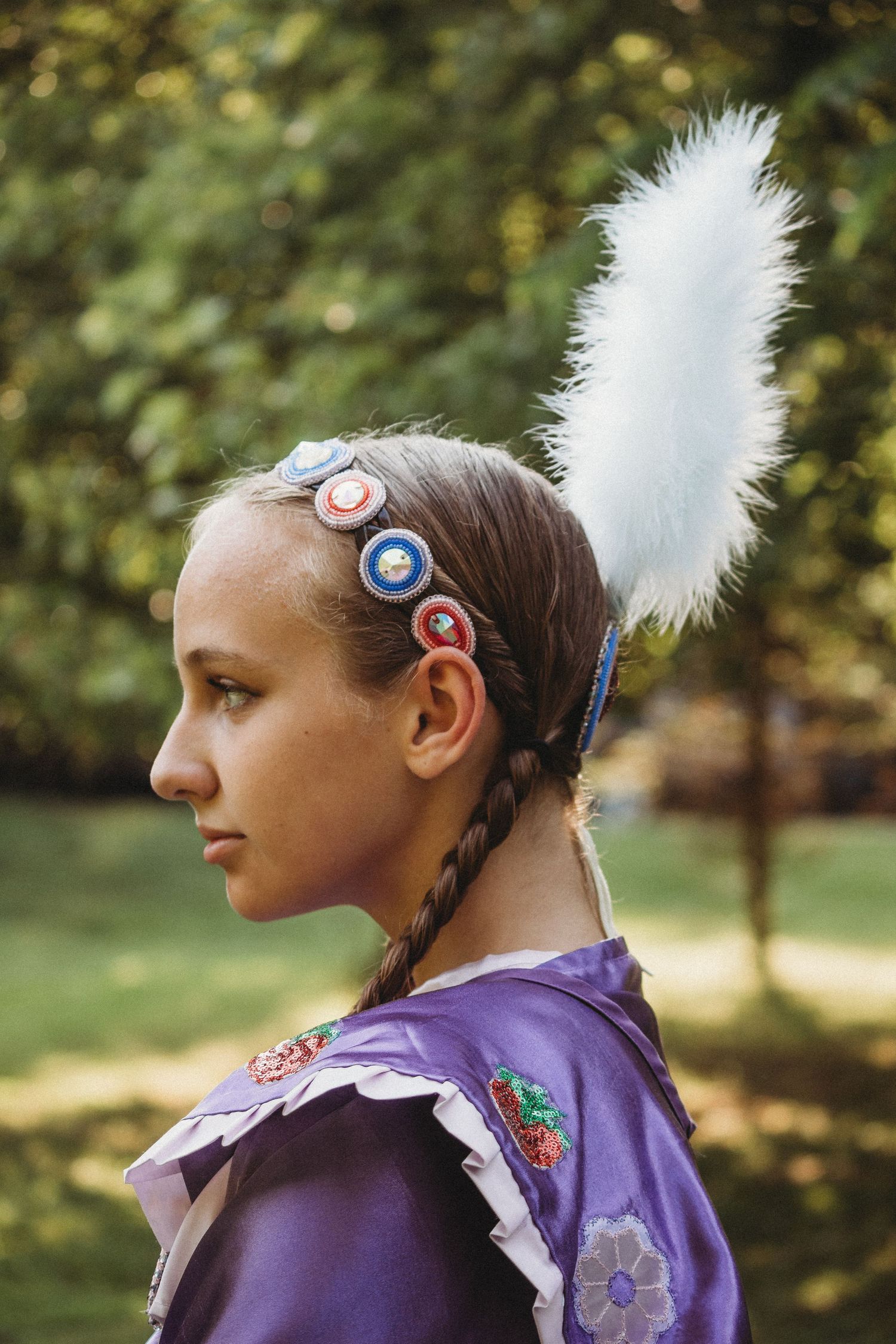 Traditional Native American regalia detail showing white feather and beaded headband against nature backdrop.