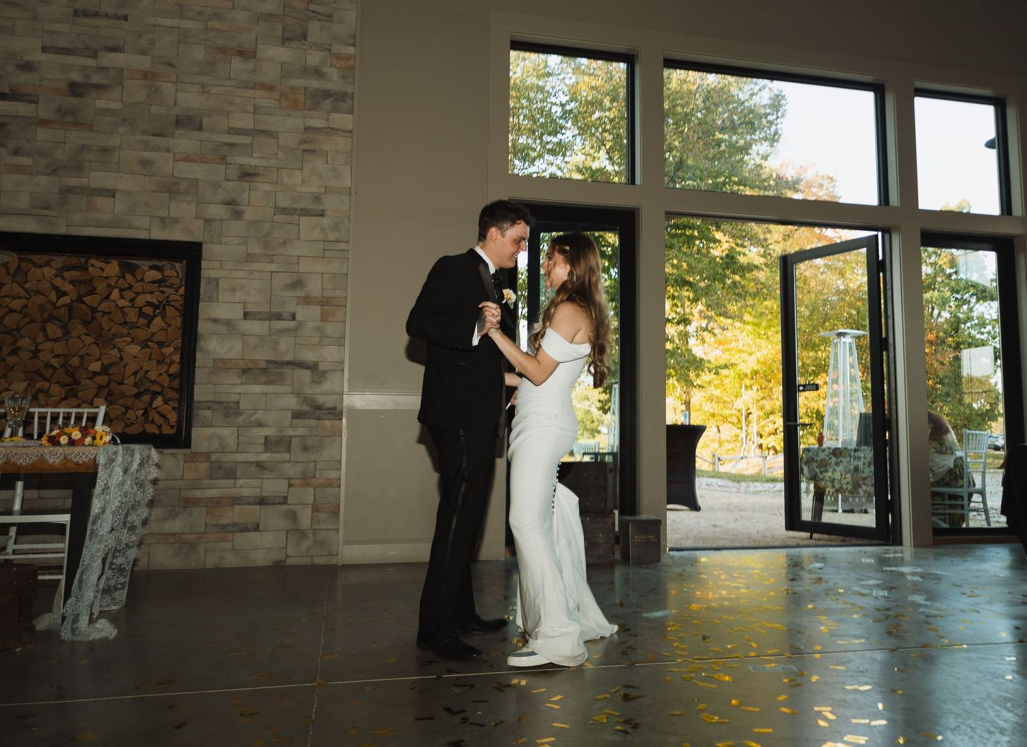 Couple shares intimate moment in modern venue with stone walls and large windows.