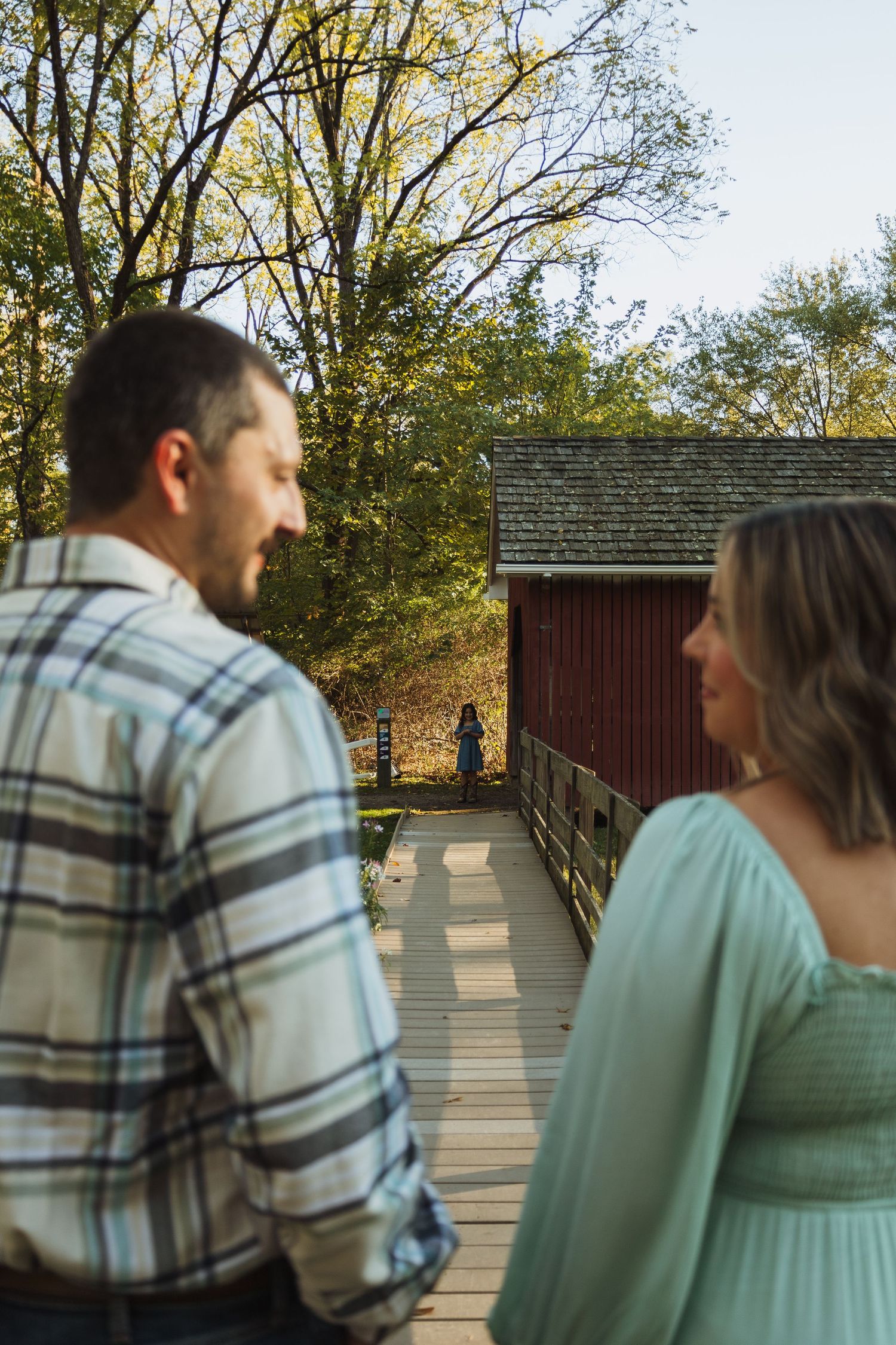 A couple in casual attire share a tender moment on a wooden bridge surrounded by autumn trees.