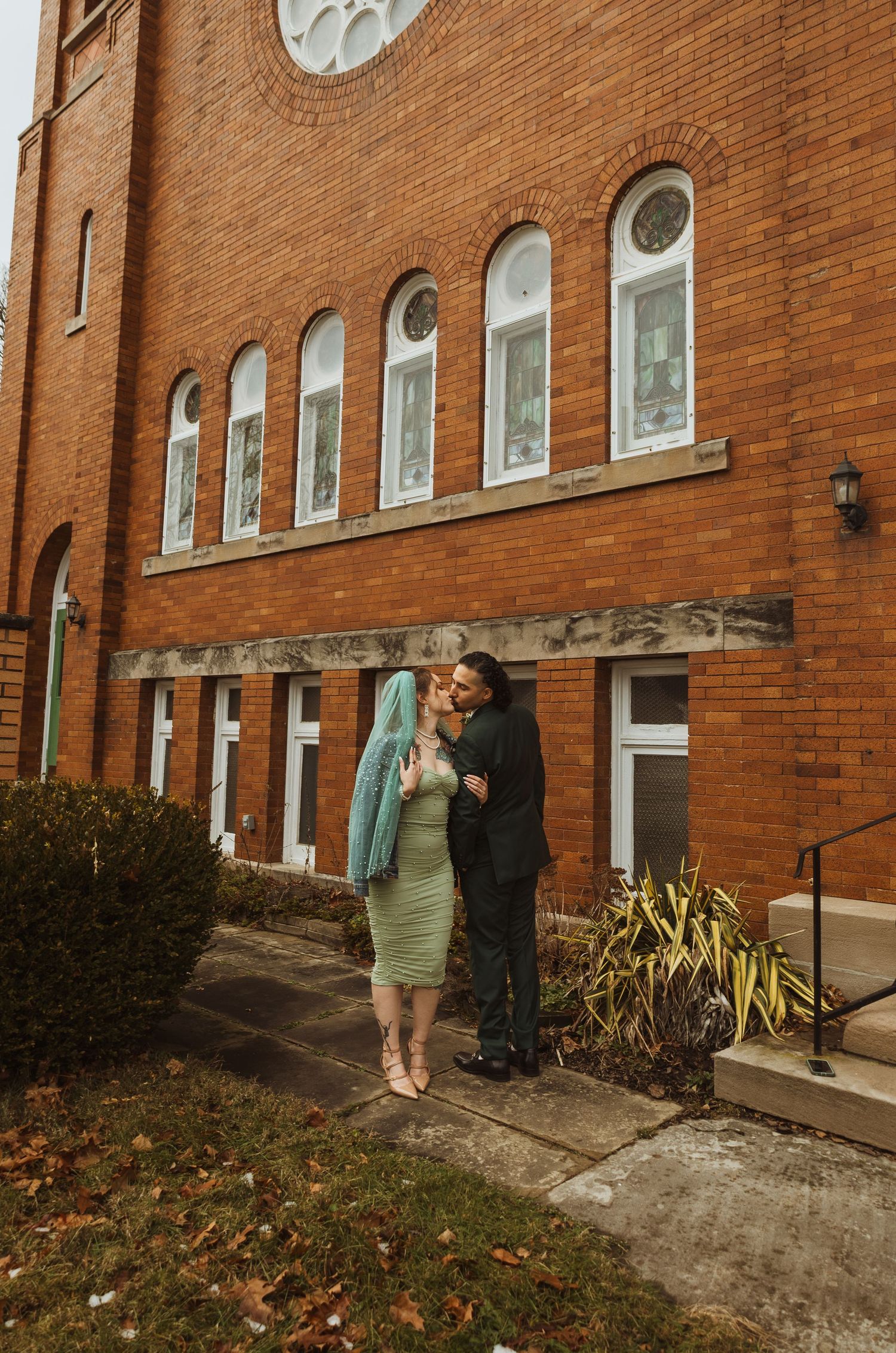 Newlywed couple kissing outside a historic red brick church on their wedding day.