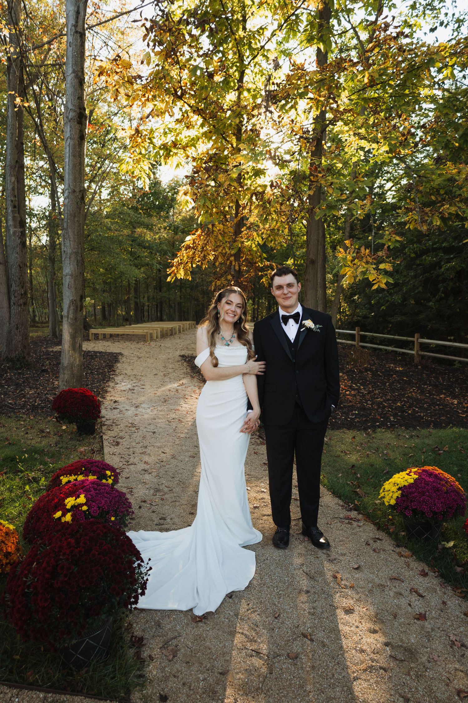 Wedding couple standing on autumn path decorated with red and yellow mums.