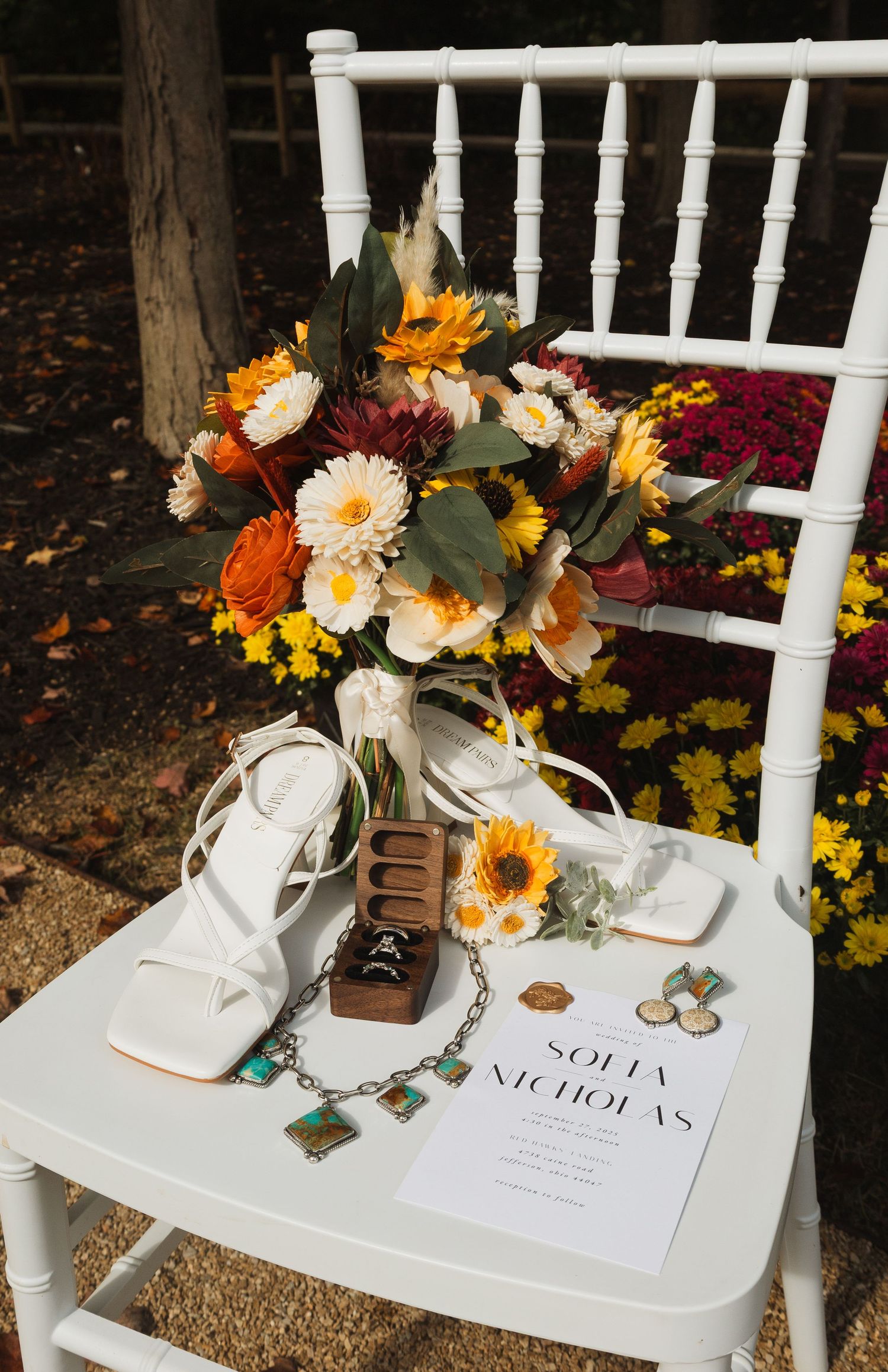 Wedding detail shot of white chairs with autumn floral arrangements and personalized place settings.