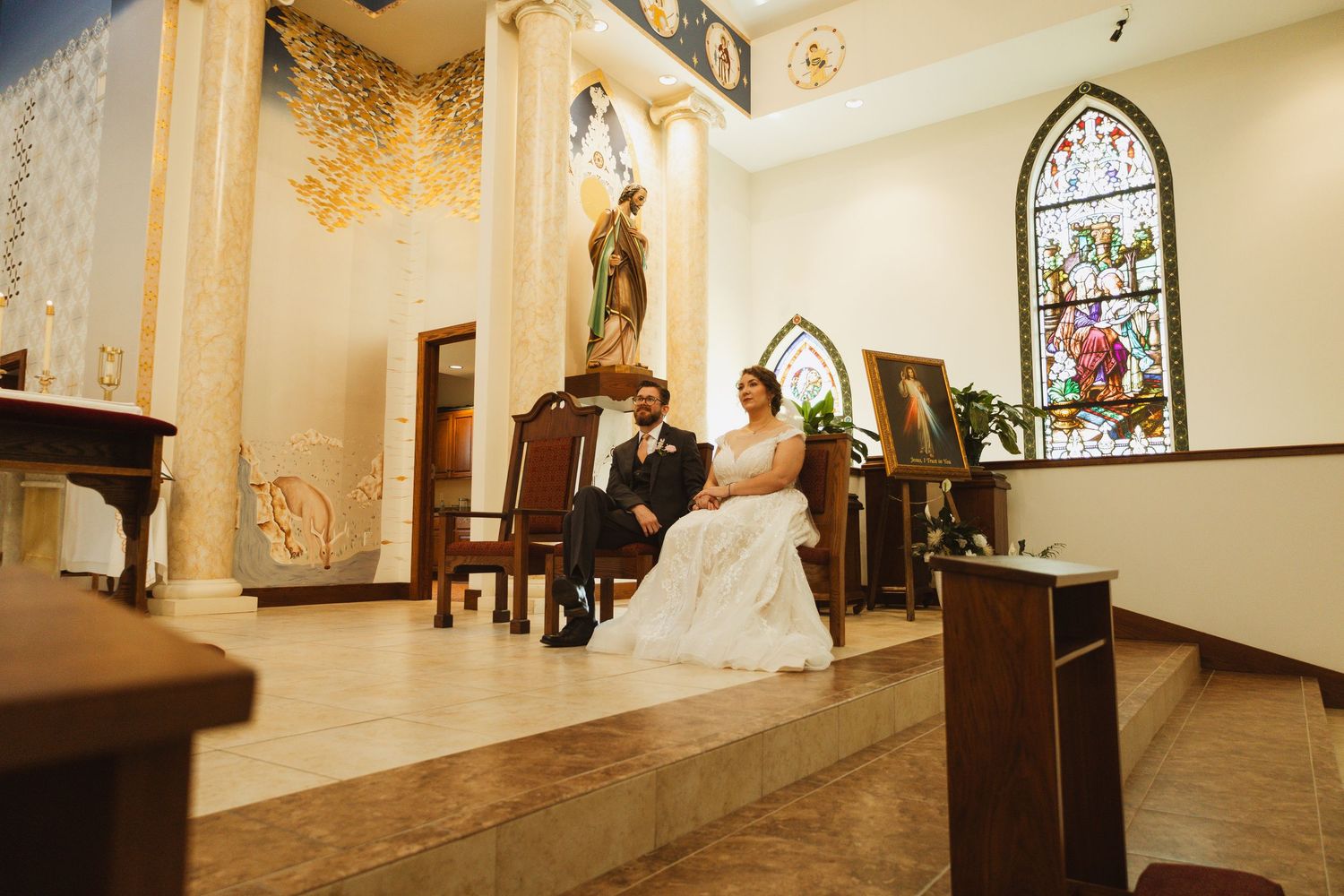 A wedding ceremony in a bright church sanctuary with stained glass and cream colored walls.
