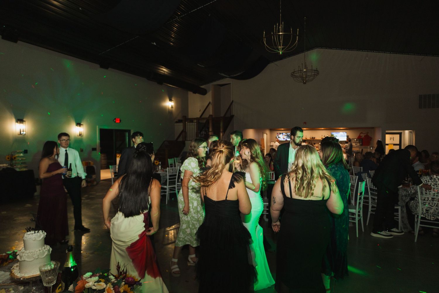 Party guests dancing under green lighting at a wedding reception.