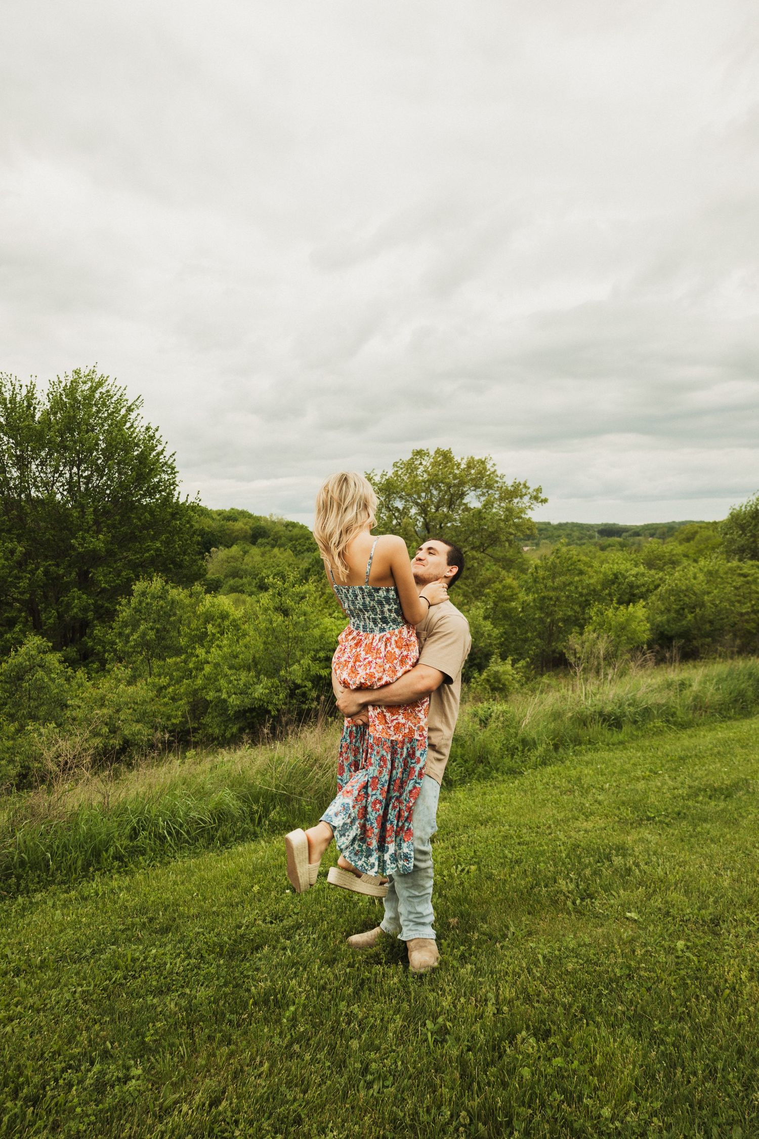 A tender moment captured of a couple dancing together on a grassy hilltop under cloudy skies.