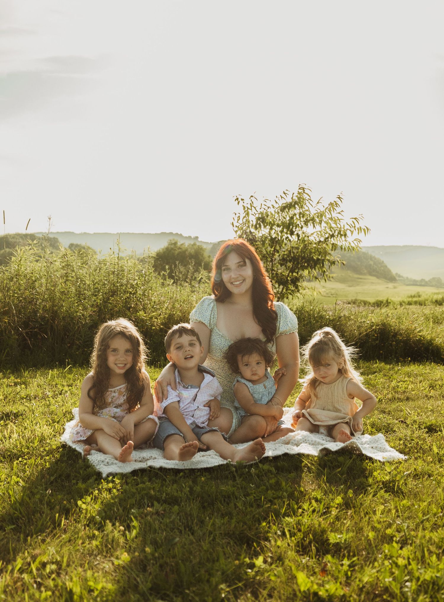 A group relaxes together on a picnic blanket in a golden meadow during sunset.