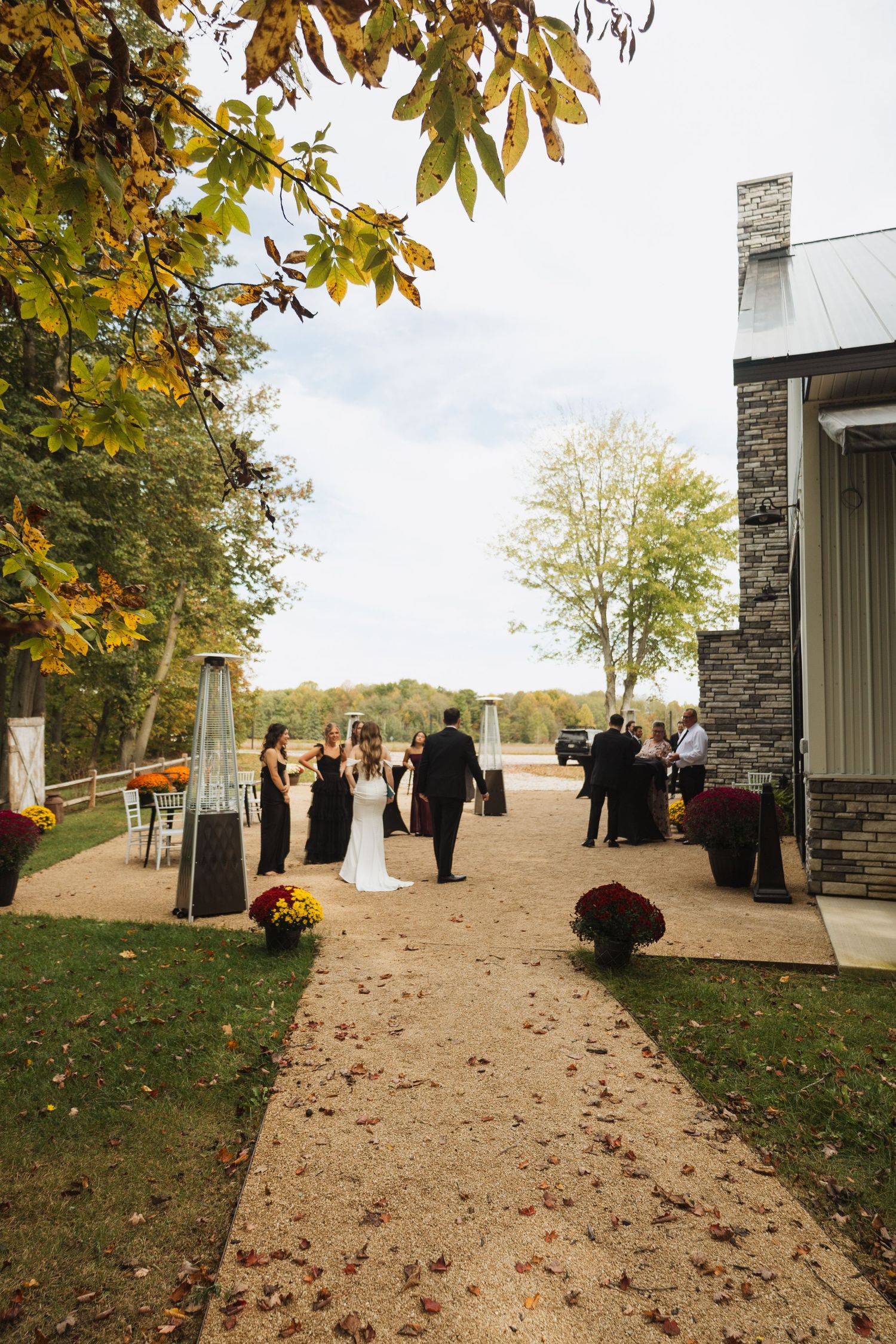 Wedding guests gather outside a stone building with autumn foliage creating a scenic backdrop.