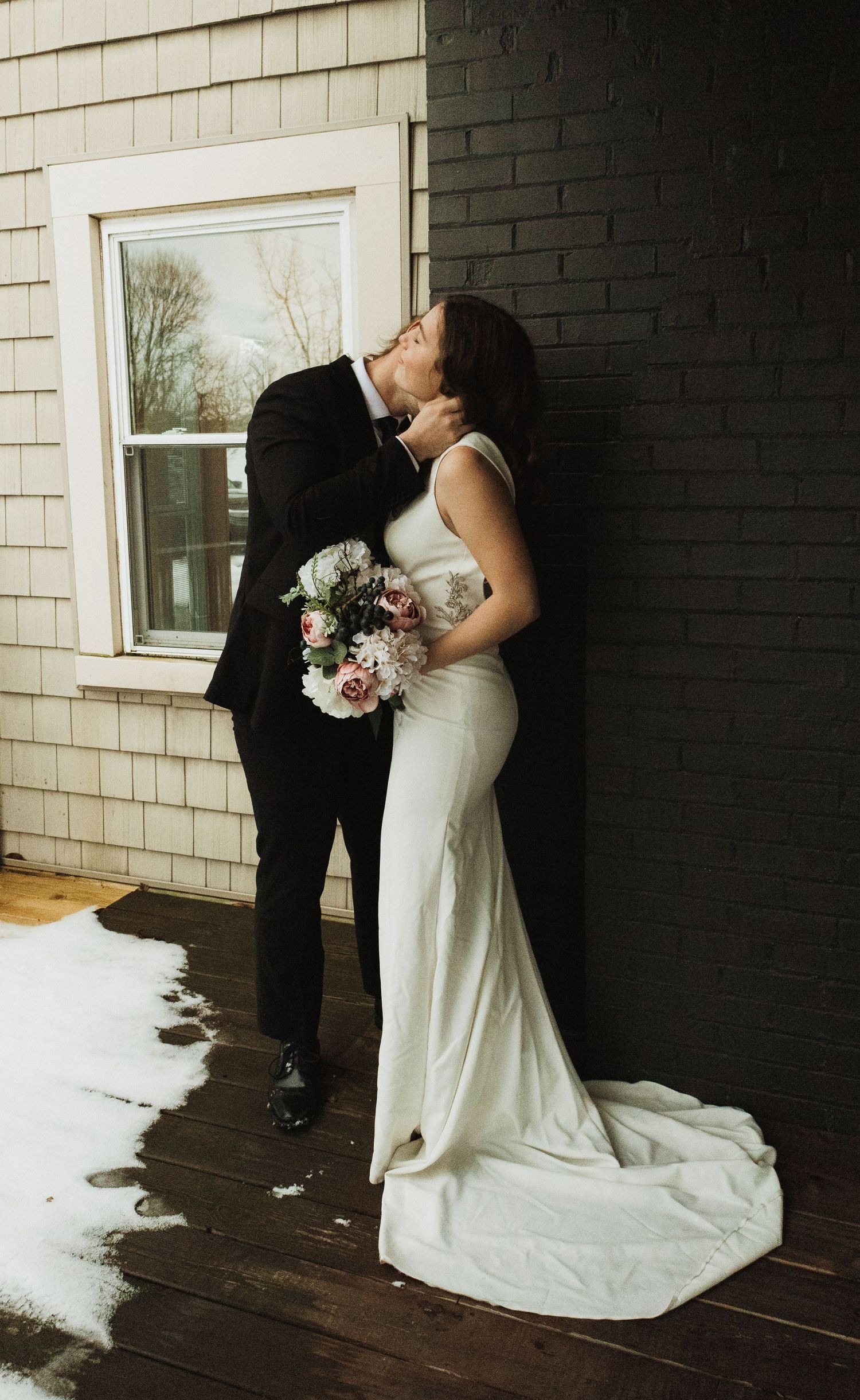 A couple in wedding attire sharing an intimate moment against a black and white exterior wall.
