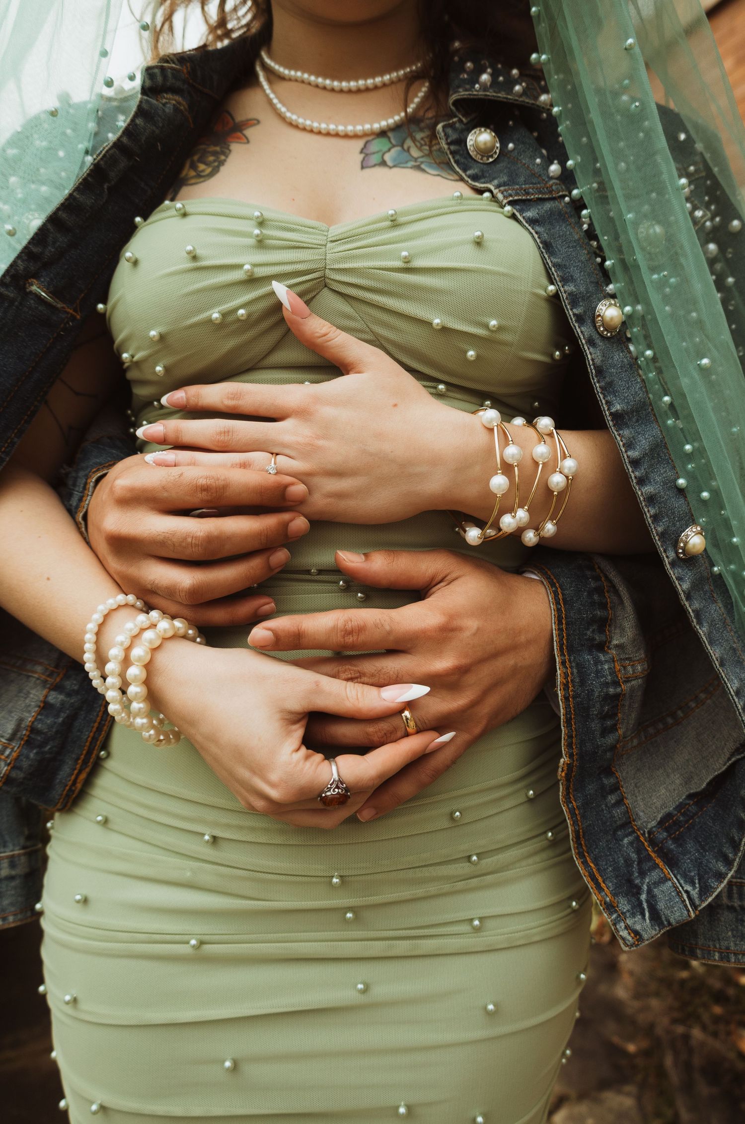 Close-up of couple's hands on bride's pearl-embellished sage green wedding dress with pearl jewelry.