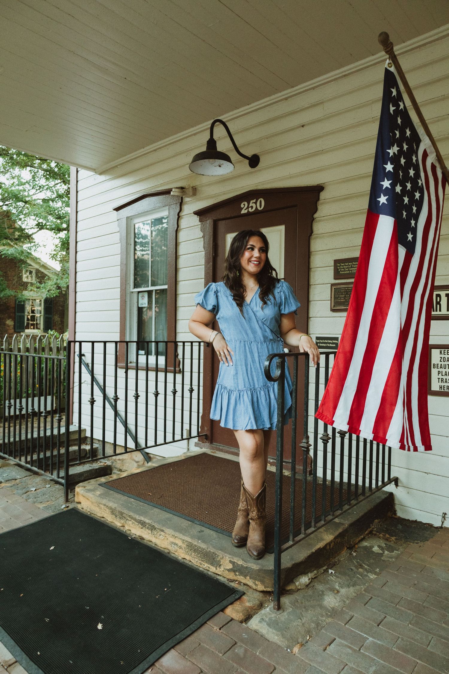 White porch with American flags displayed features rustic decor and brick pathway.