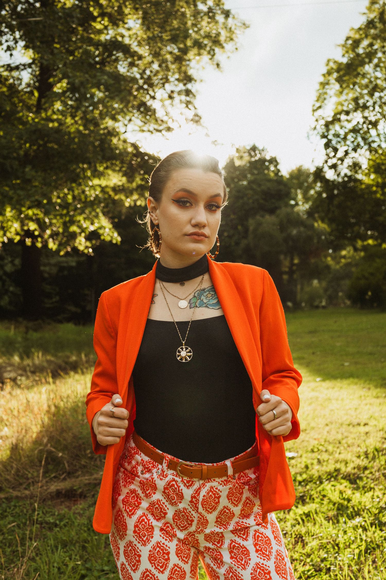 Stylish outfit featuring bright orange jacket and patterned pants captured in golden sunset light.
