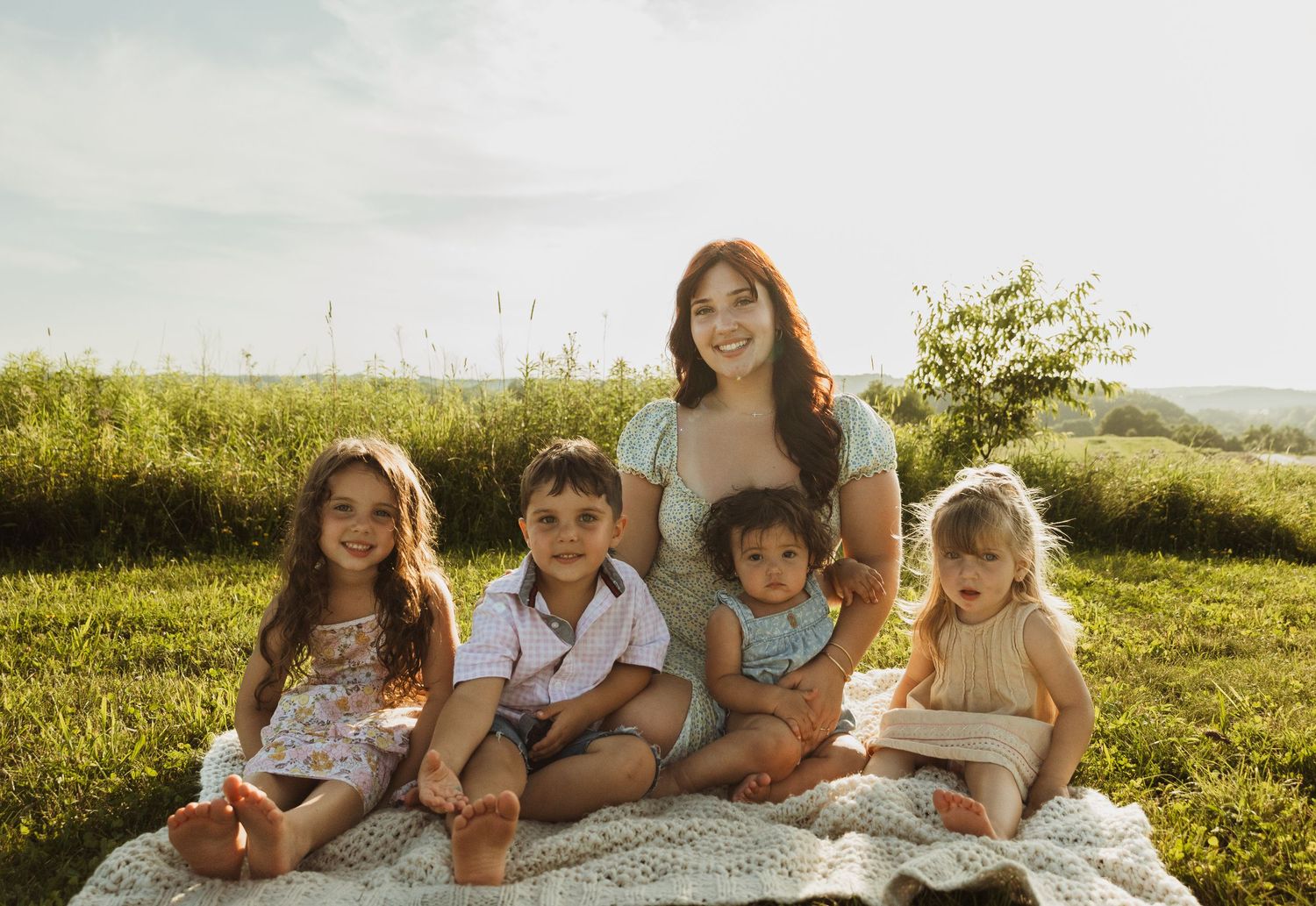 A group sits together on a blanket in a sunny field during golden hour for a photo session.