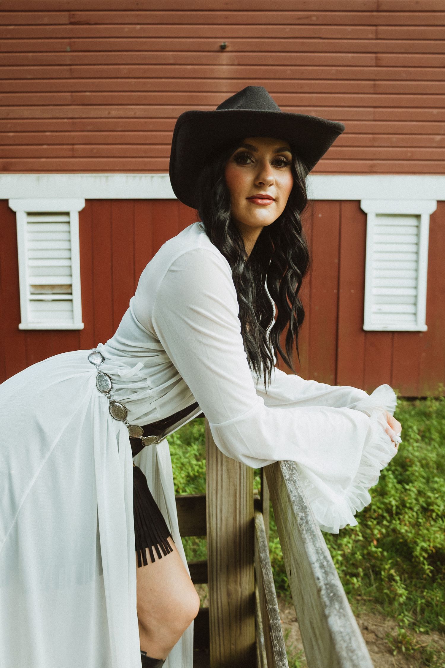 Fashion photo series showing someone in a white bell sleeve dress and dark wide-brimmed hat posing against a red barn wall.
