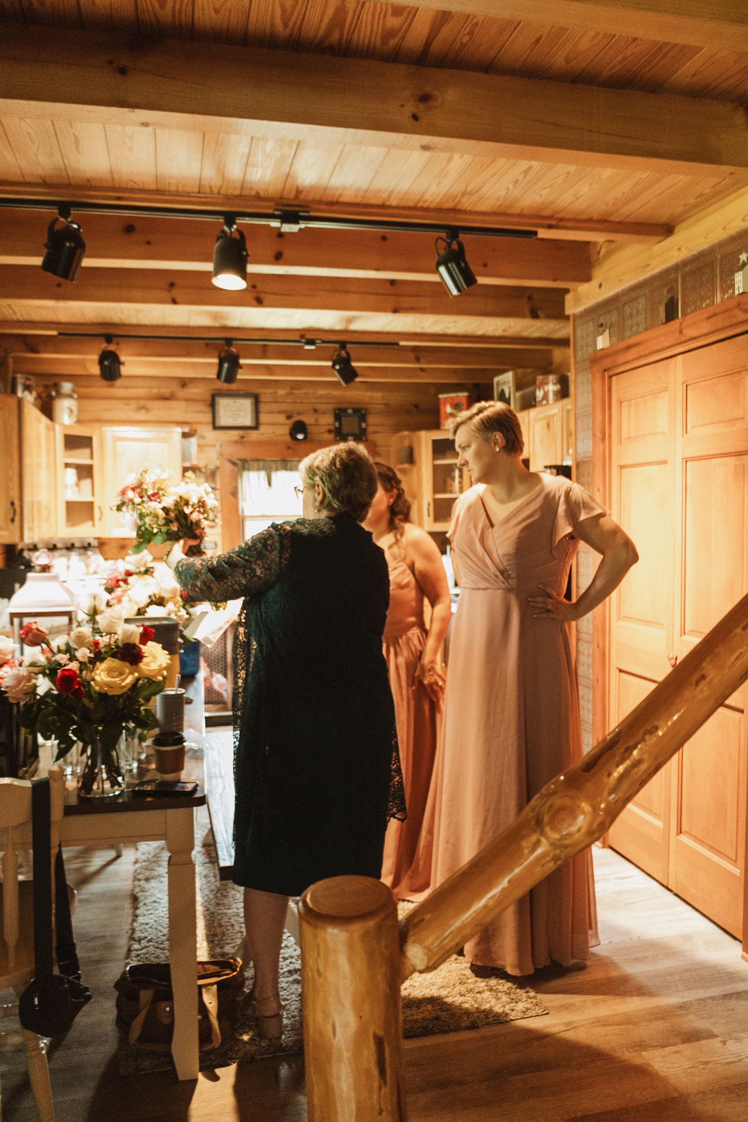 Wedding party members gather in a rustic wooden room with exposed beams and track lighting.