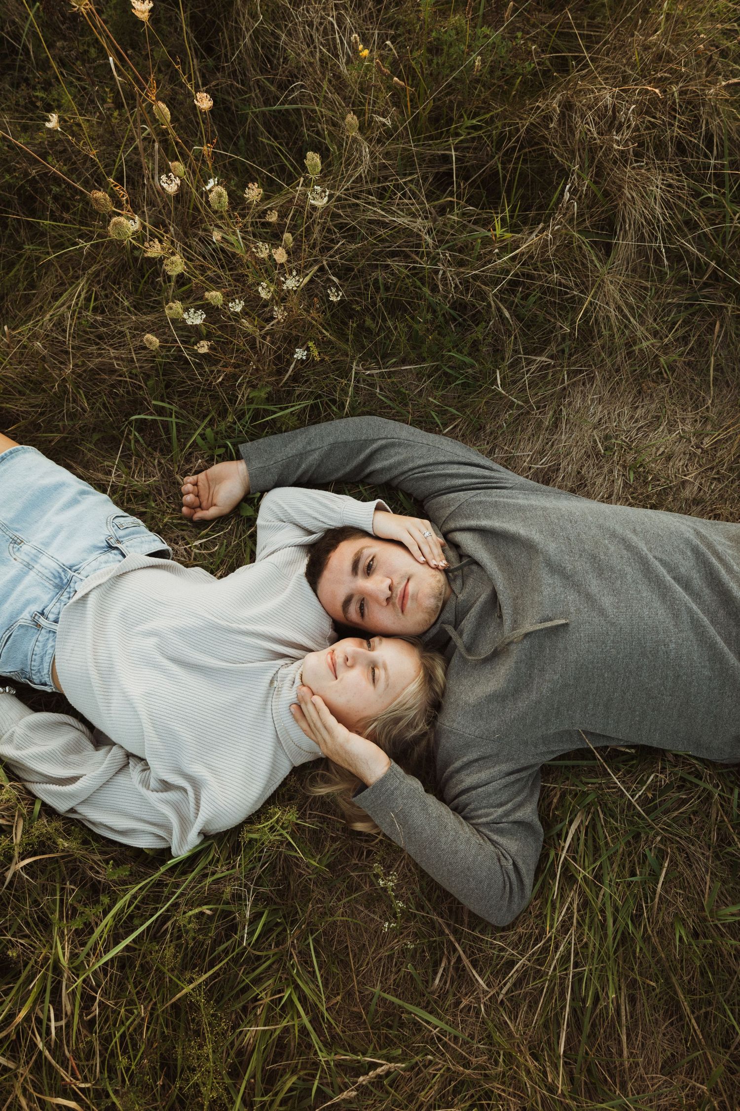 Couple shares intimate moment laying in dry grass during sunset.