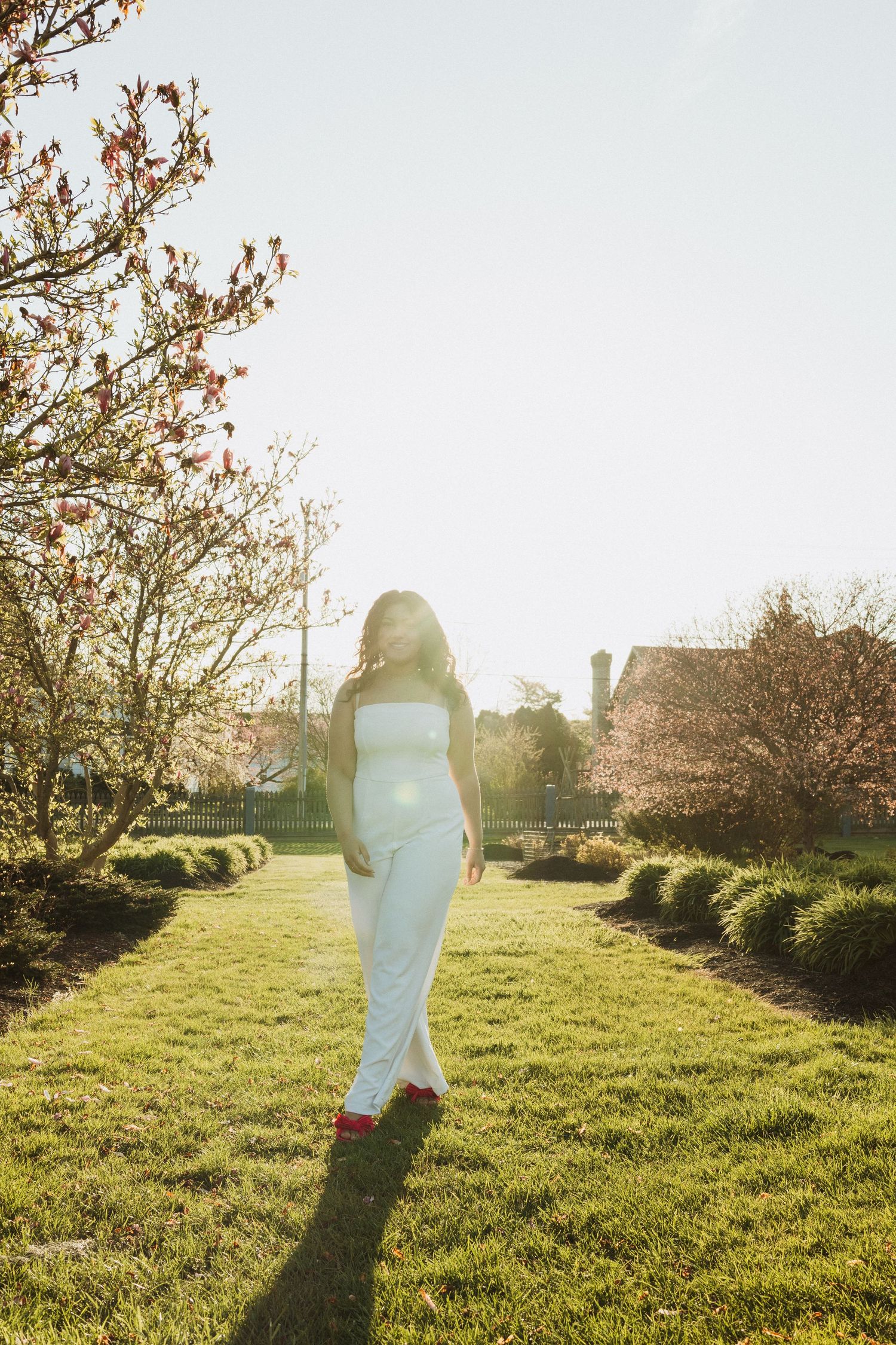 A silhouette of a person in white walking through a sunlit garden path.