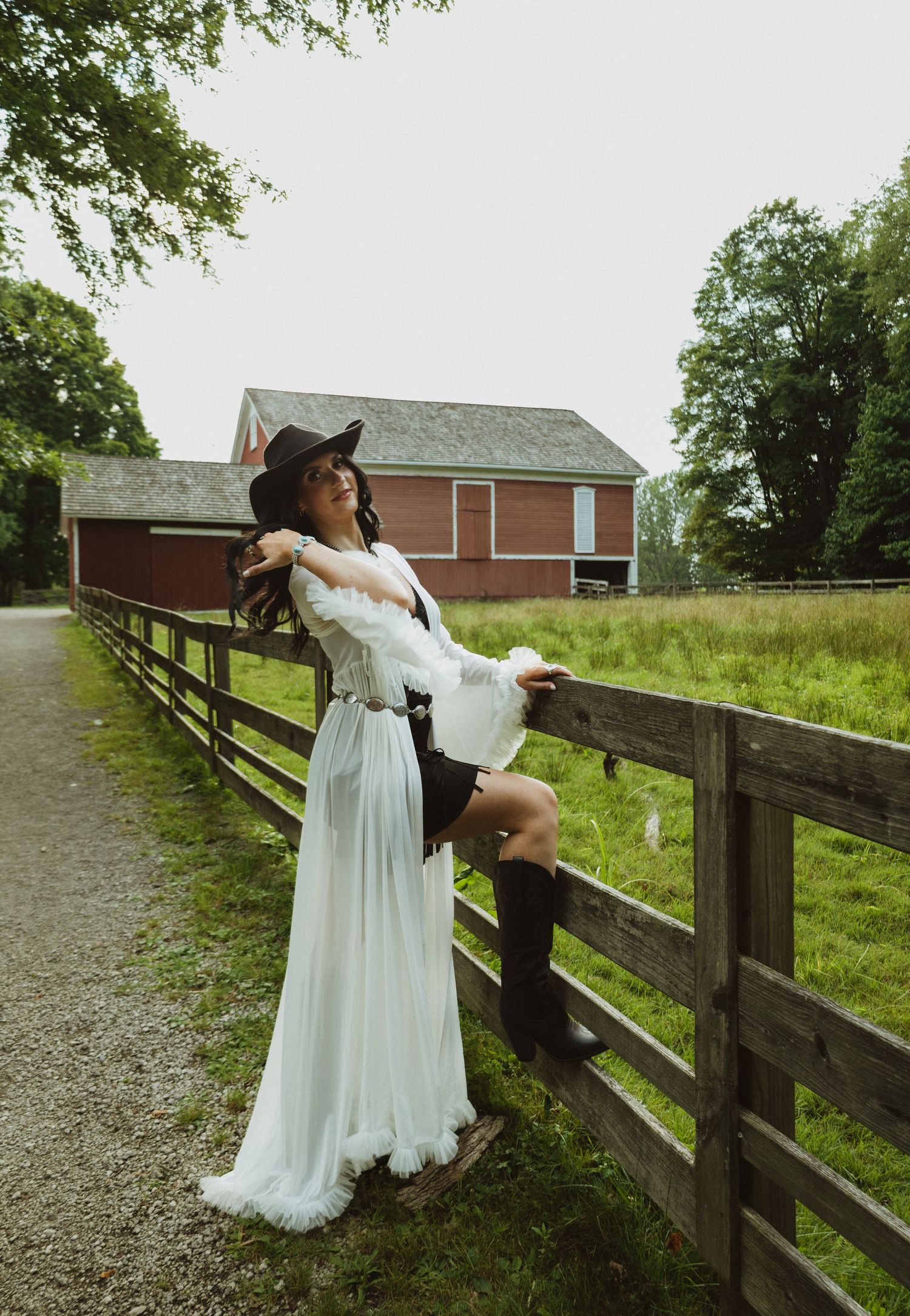 A flowy white dress and cowboy hat create a western-chic look against a rustic wooden fence and barn backdrop.
